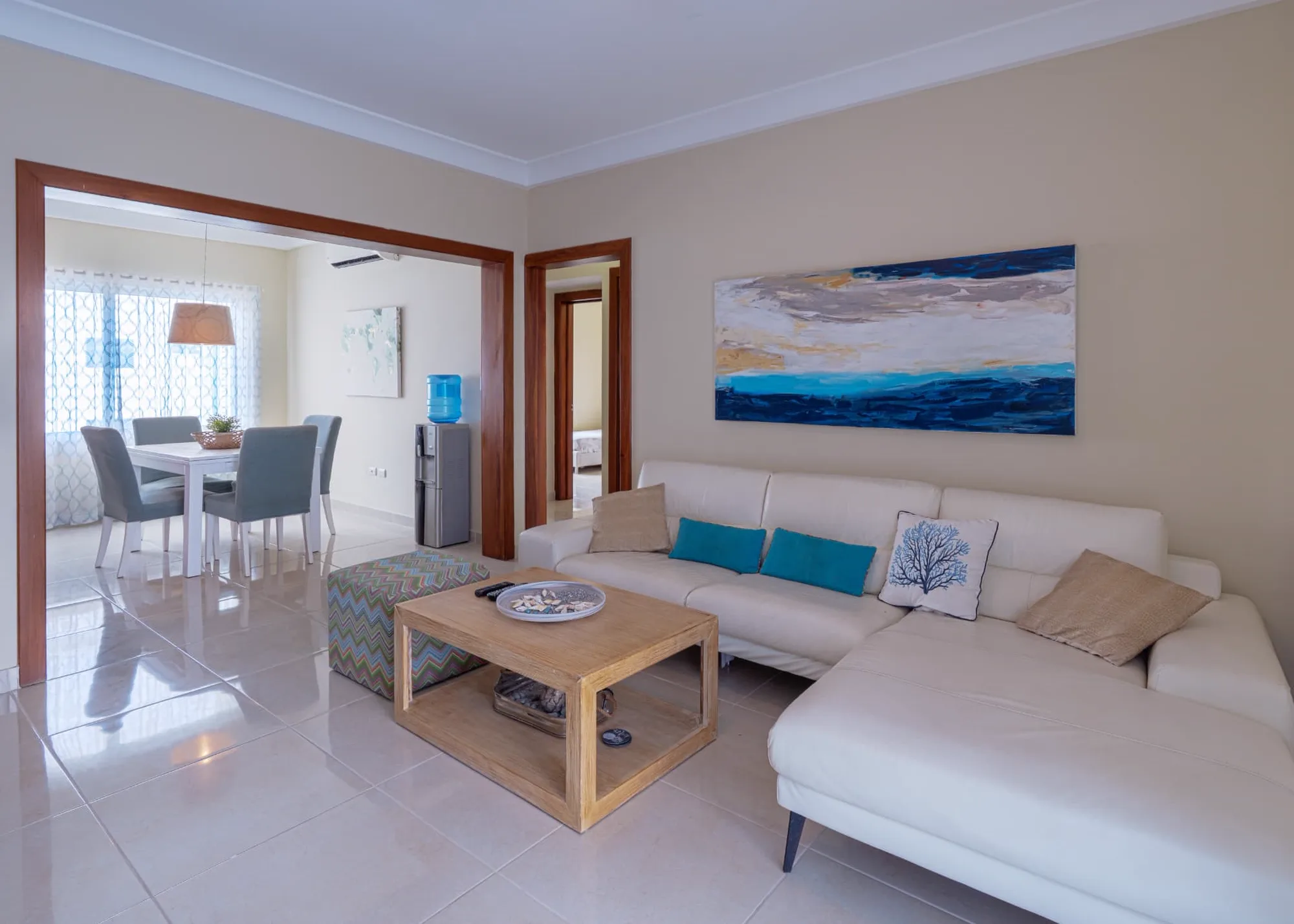 Open living room at Eden with white leather sectional, ocean artwork and the dining area beyond