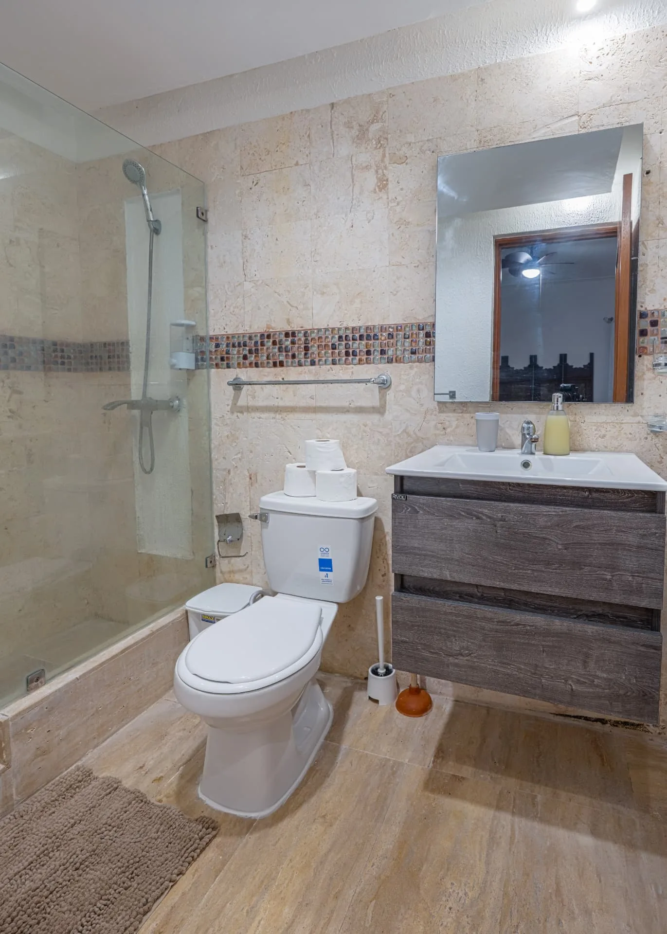 Bathroom clad in travertine with mosaic tile band, glass walk-in shower and a floating timber vanity