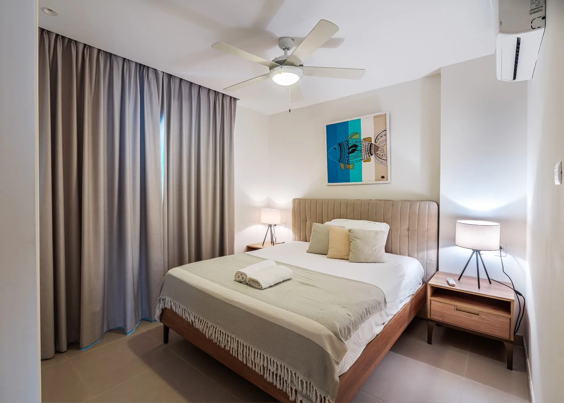 Primary bedroom with tufted headboard, matching tripod lamps and coastal artwork above the bed