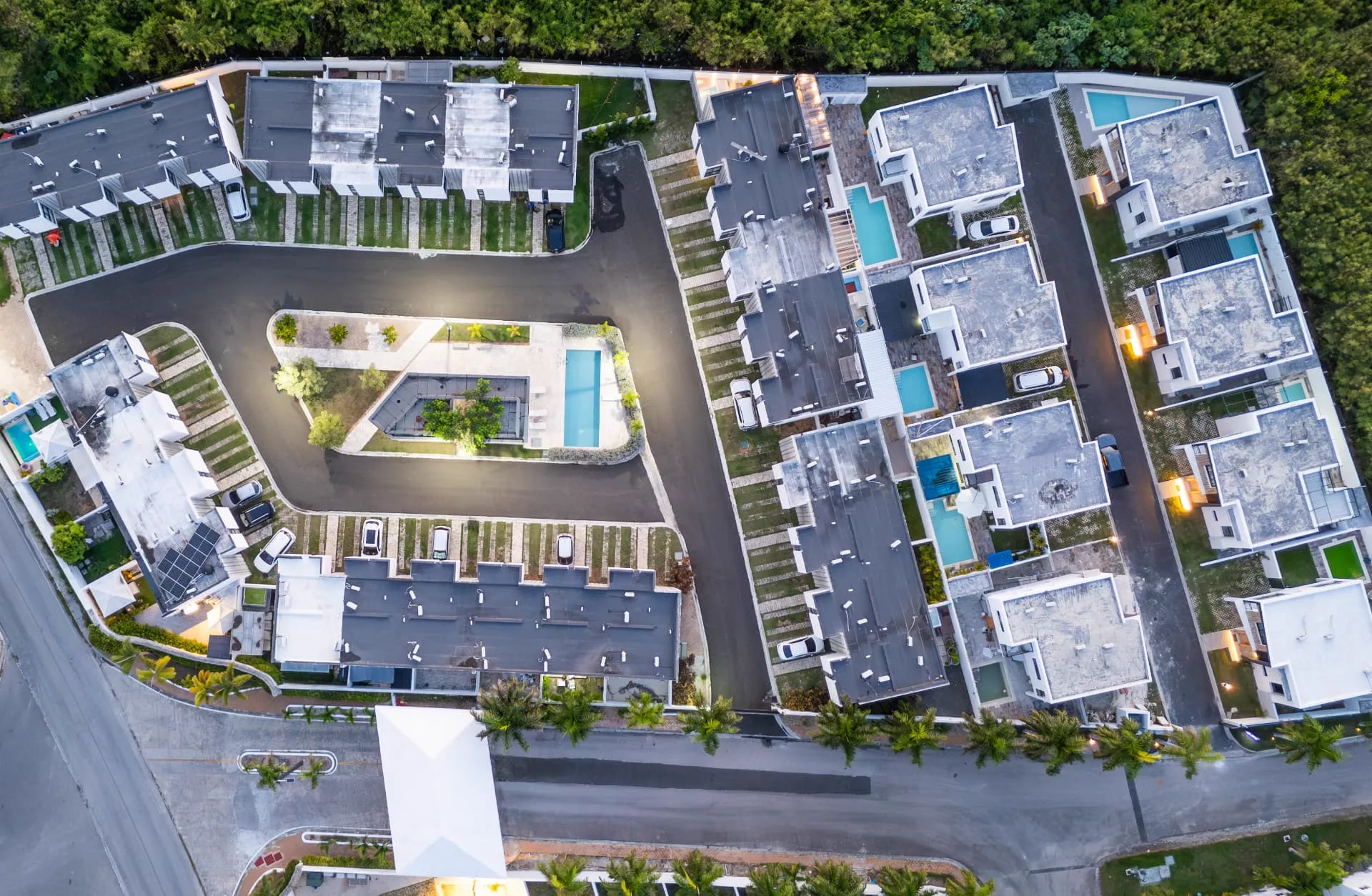 Overhead drone view of the White Sand gated community at dusk showing townhouse rows, private plunge pools, villas and the central pool courtyard