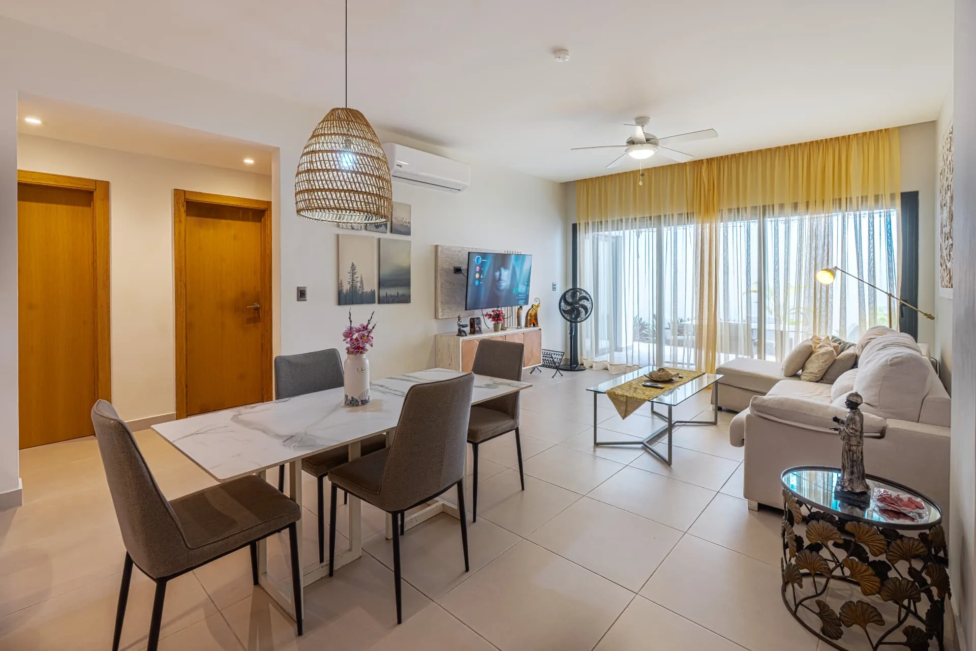 Living and dining area with marble dining table, rattan pendant light, wall-mounted TV and sheer curtains onto the terrace