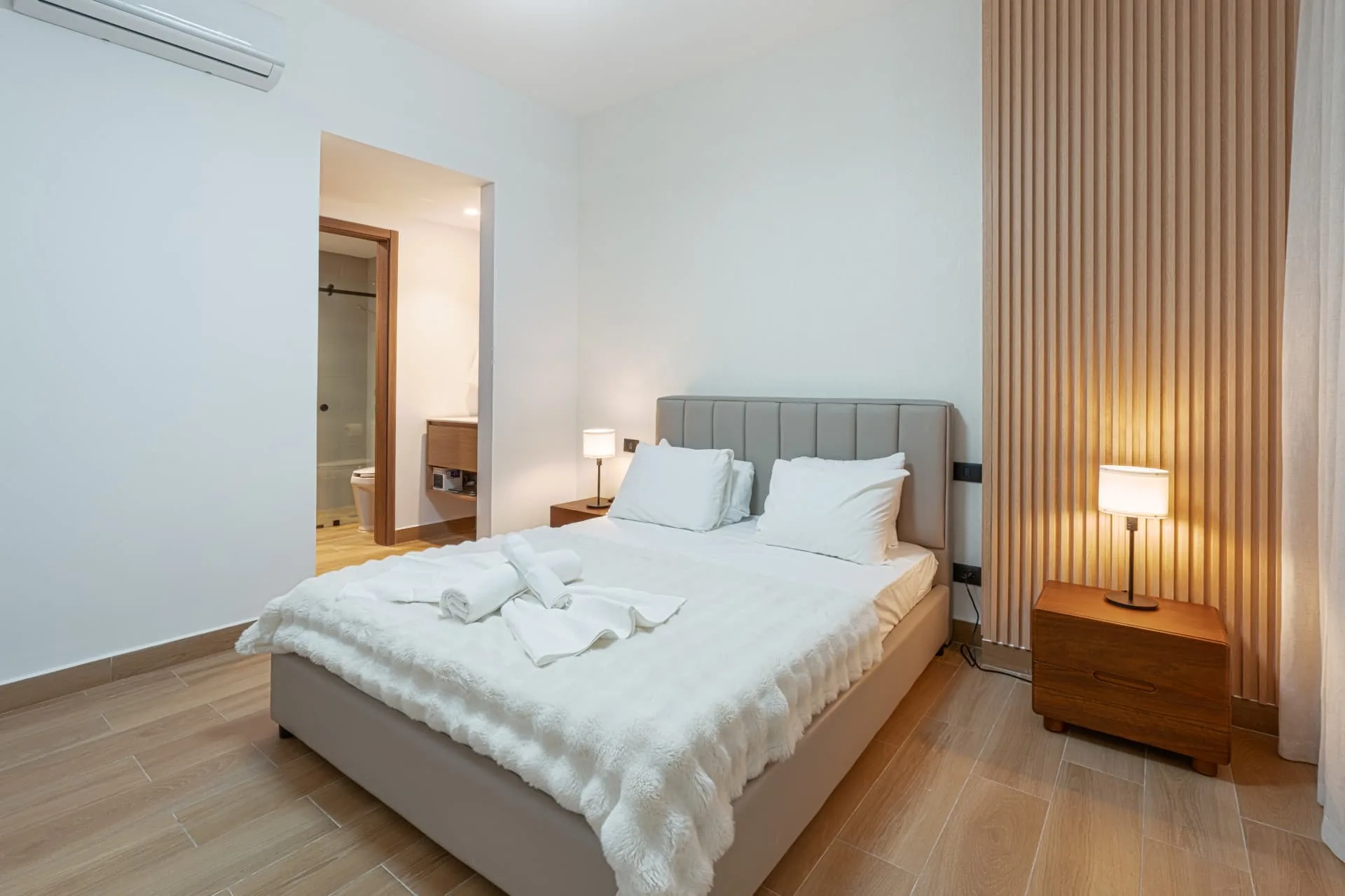 Bedroom with slatted timber feature wall, warm lamp light and an adjoining en-suite bathroom