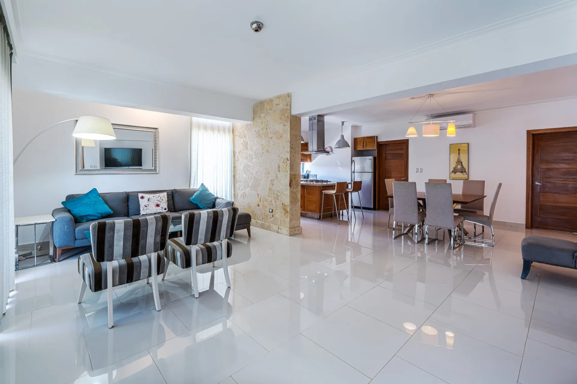 Wide condominium interior with grey sectional sofa, coral stone column, dining table and hardwood kitchen