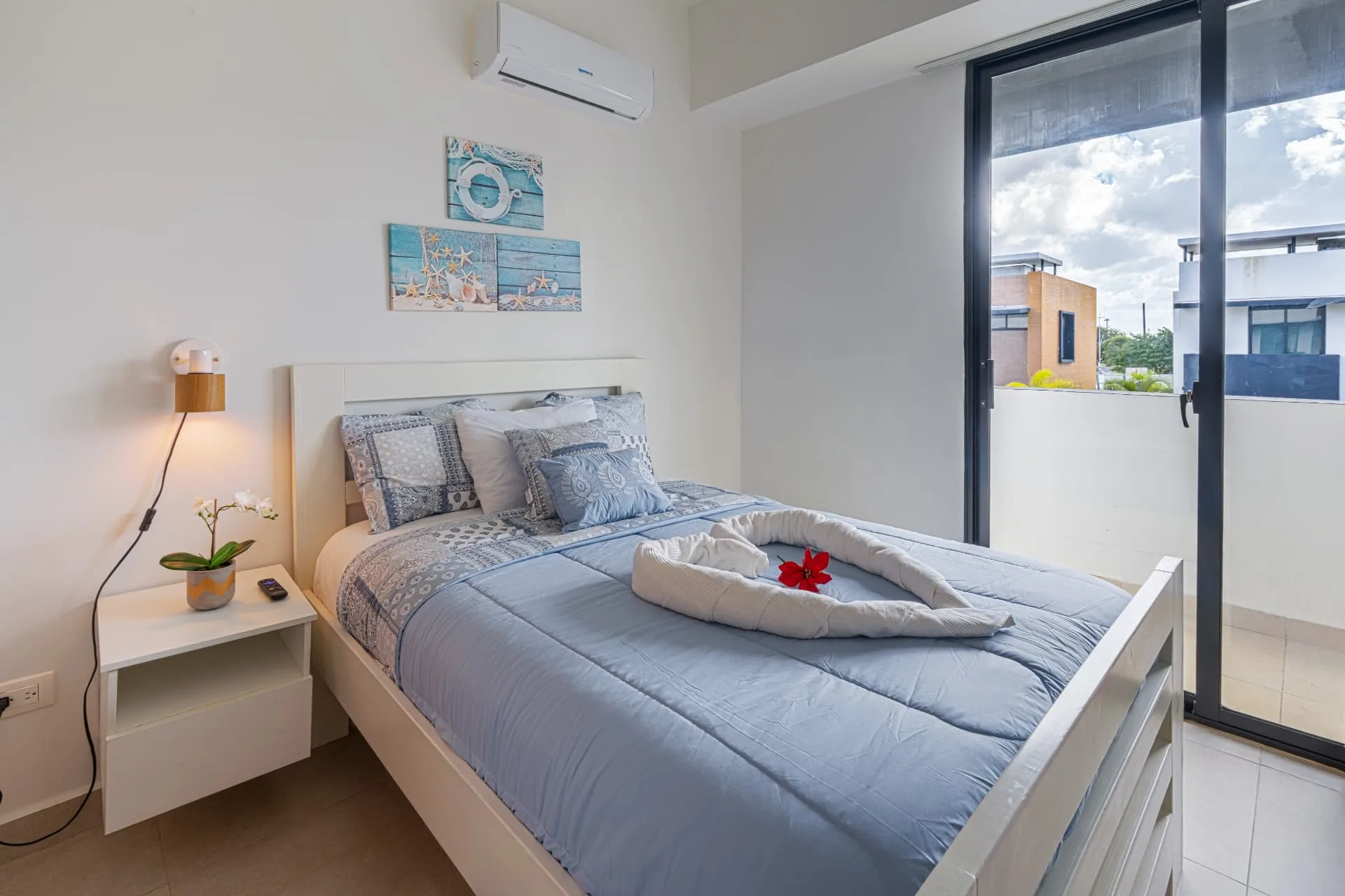 Guest bedroom with blue bedding, coastal wall art and sliding doors to a balcony