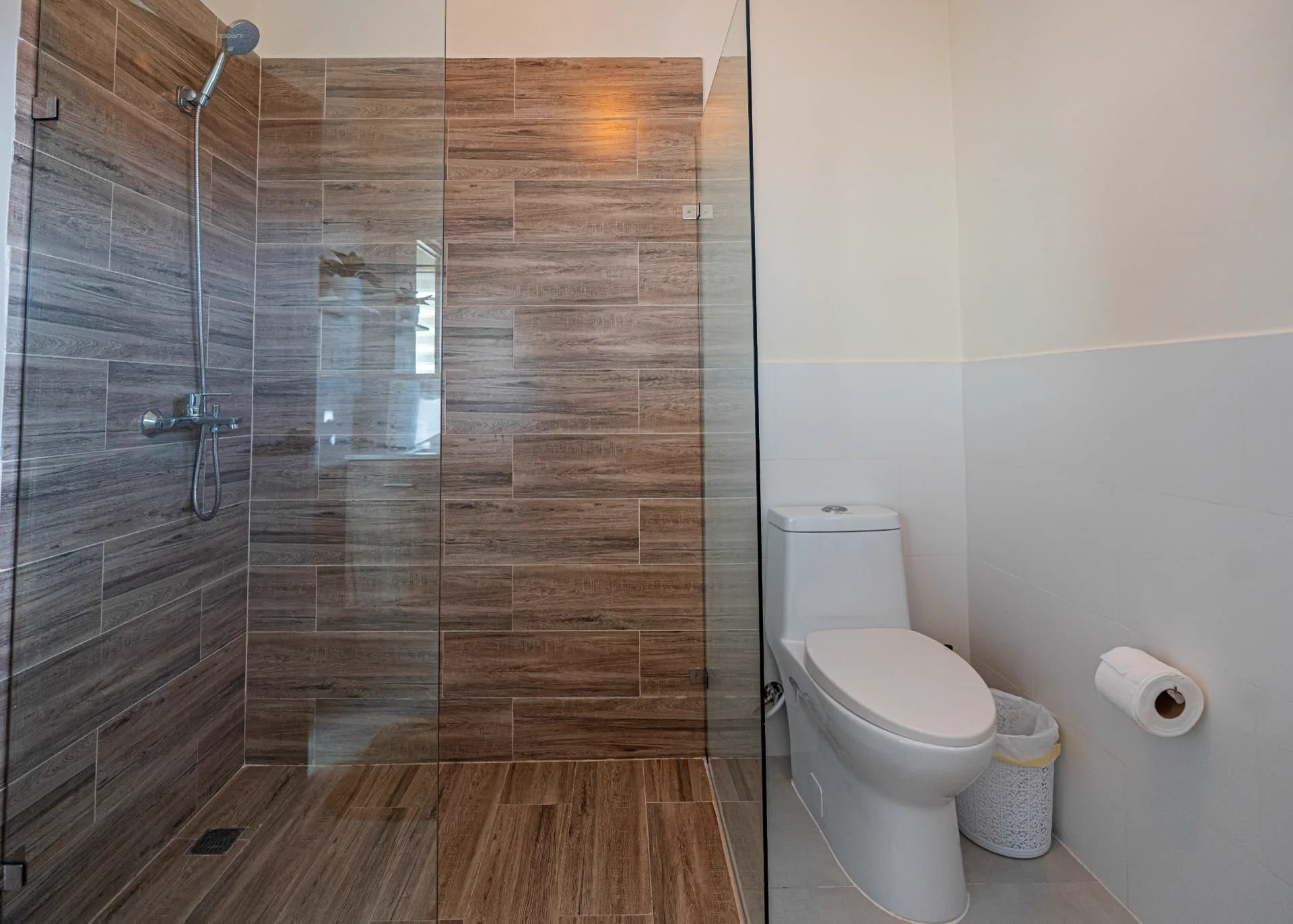 Walk-in shower clad in timber-look tile behind a frameless glass panel next to the toilet