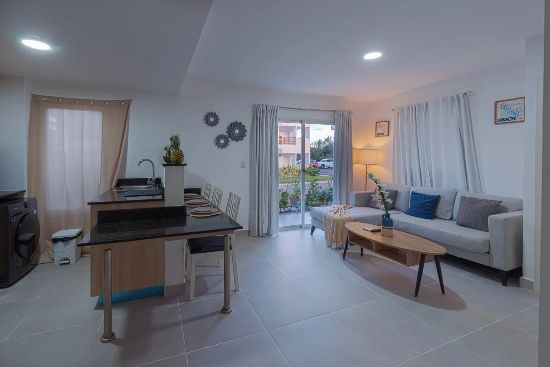 Open-plan condominium living room with grey sofa, granite dining bar and terrace doors to the garden