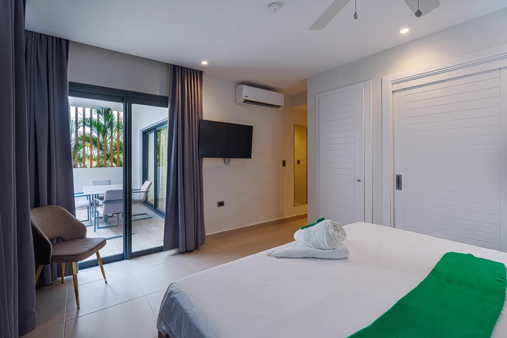 Bedroom with sliding glass doors opening to a private terrace with dining set and palms