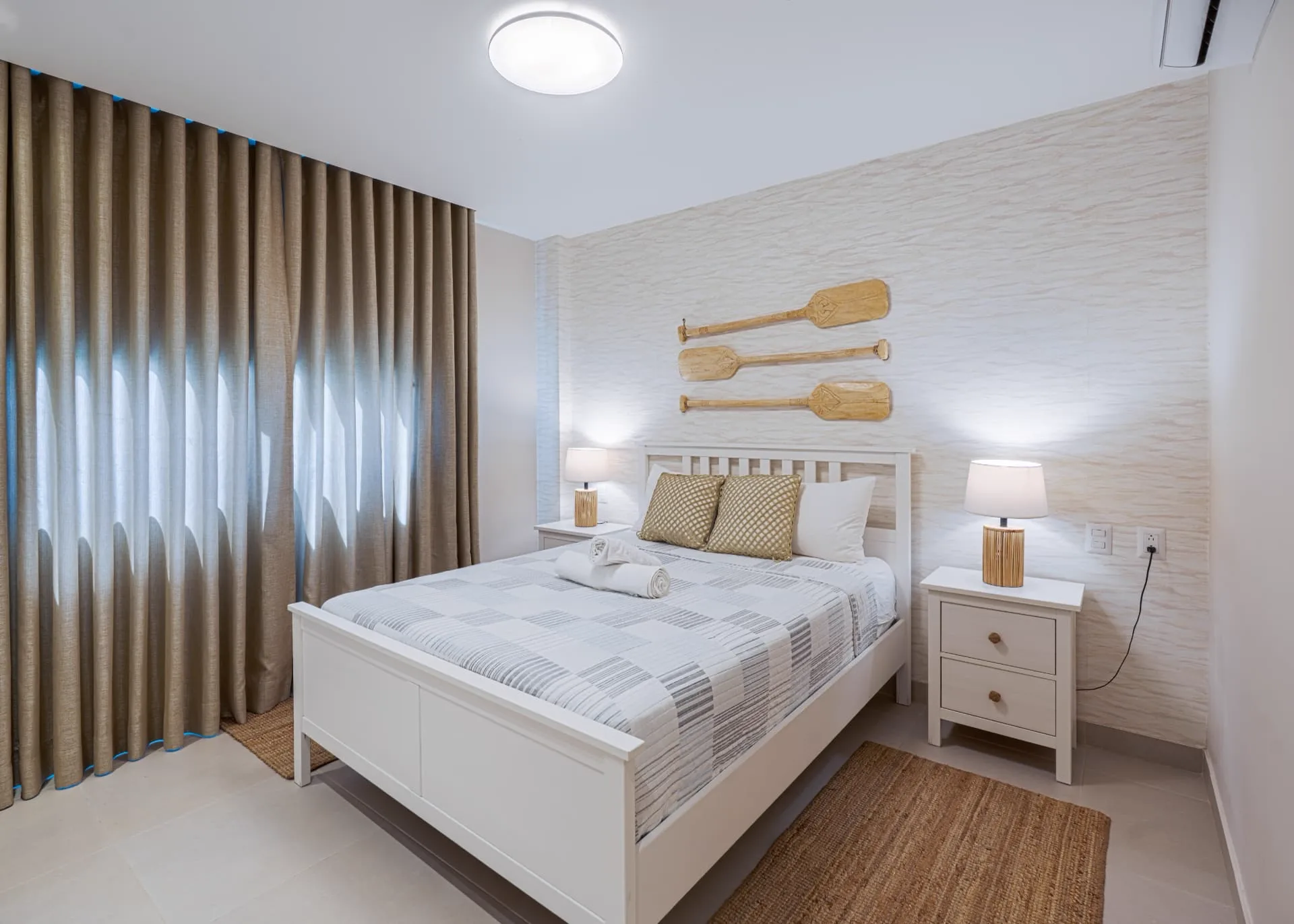 Bedroom with textured feature wall, carved wooden paddles above the bed, matching lamps and jute rug