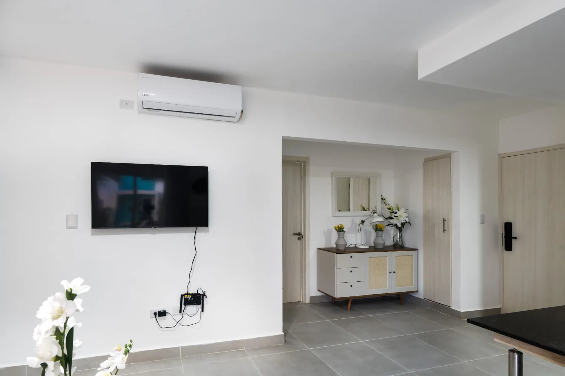 Living room media wall with mounted television and a rattan console by the entry door