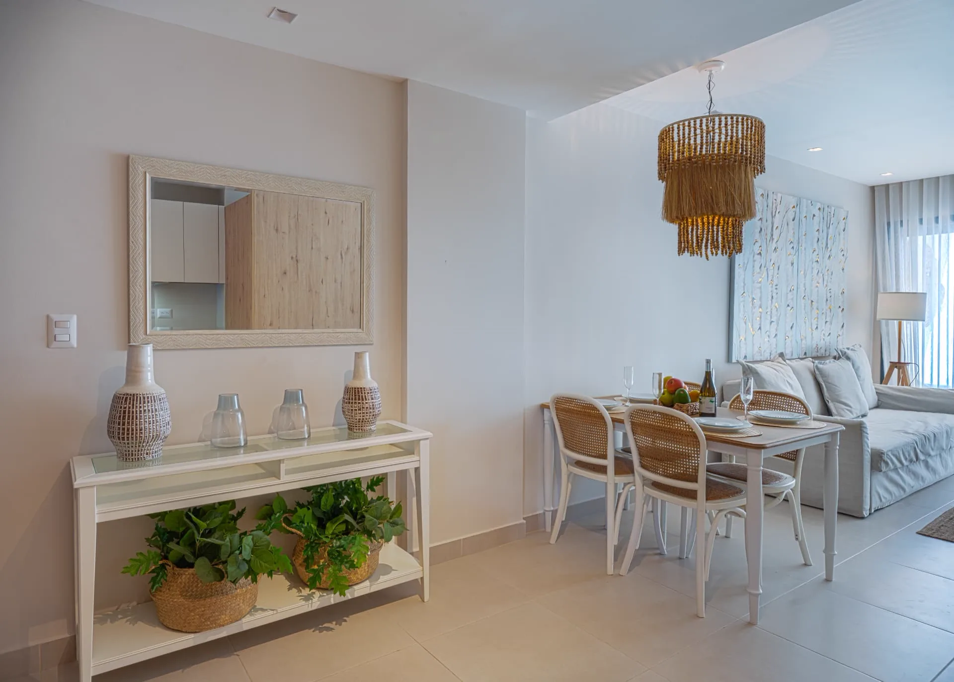 Entry console with woven vases and framed mirror beside a rattan dining set under a fringed pendant light