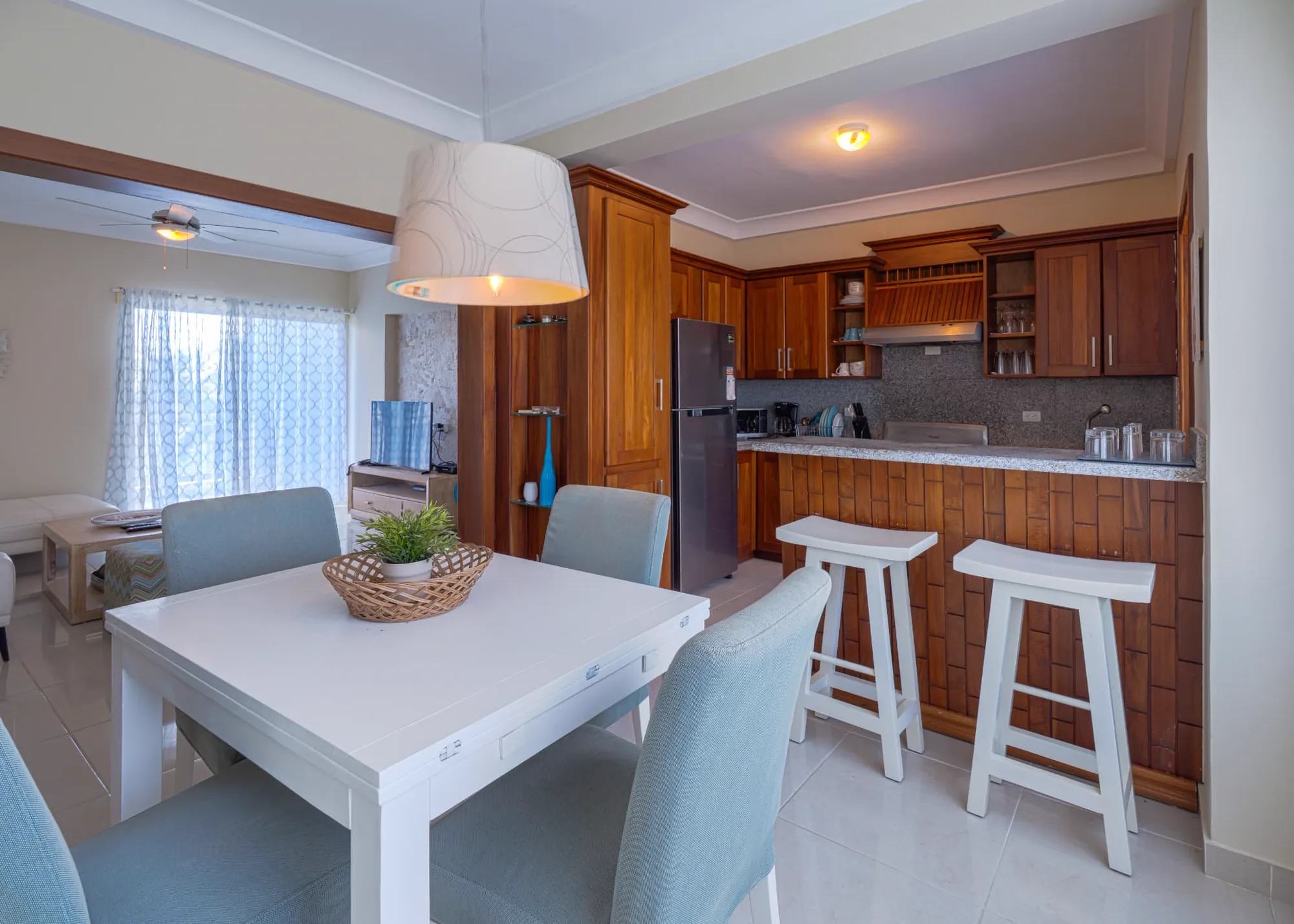 White dining table under a pendant lamp with the mahogany kitchen breakfast bar and stools beyond