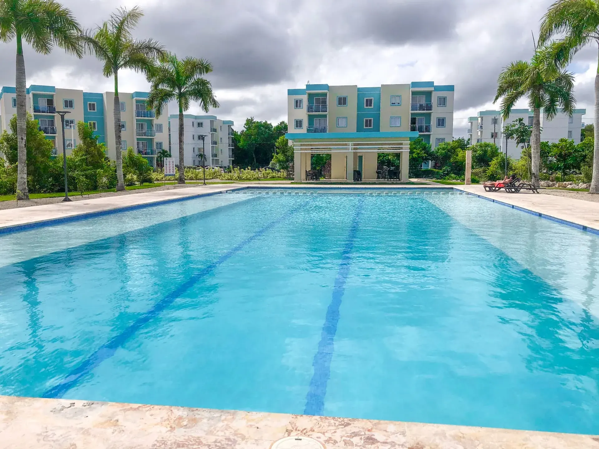 Long lap pool lined with royal palms in front of the turquoise-accented condominium blocks