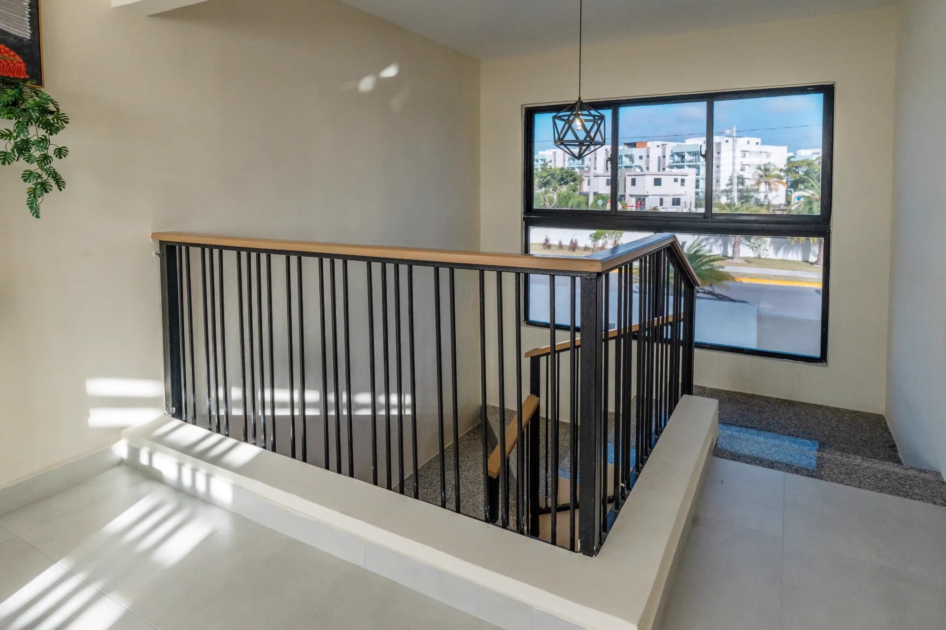 Internal staircase with black steel balustrade, timber handrail and a geometric pendant beside tall windows