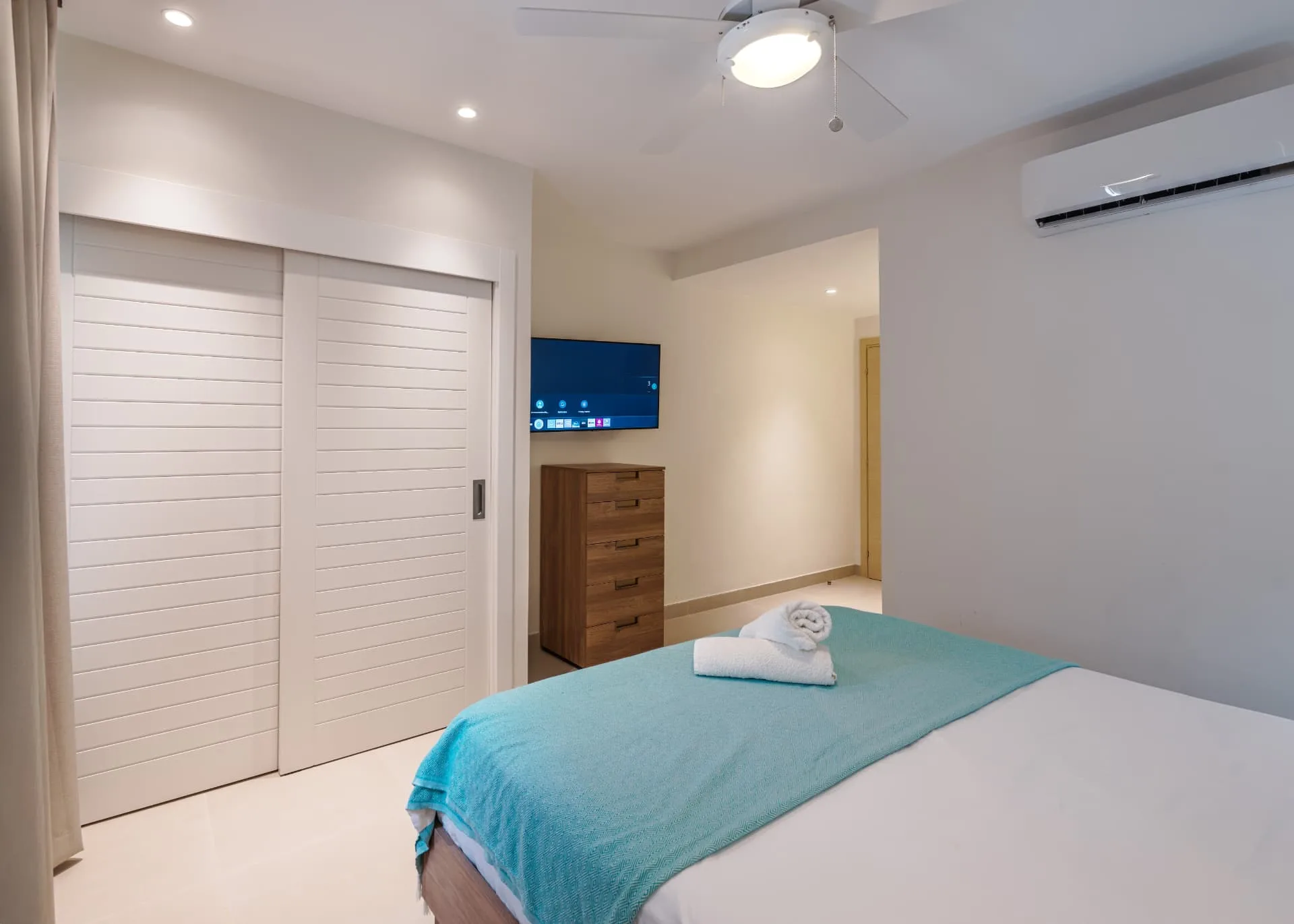 Second bedroom with turquoise throw, timber dresser, wall-mounted TV and sliding closet doors