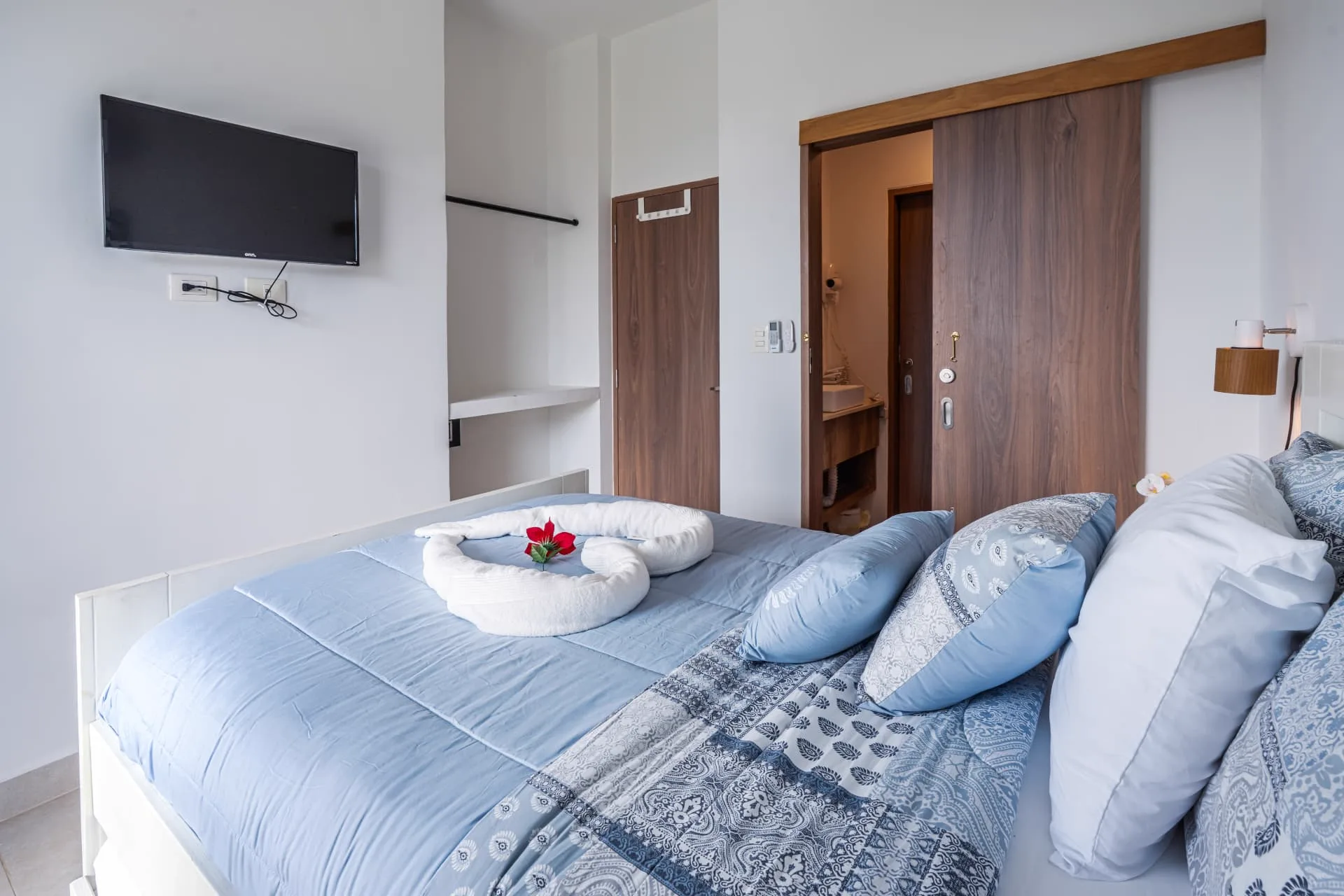 Bedroom with blue linens, wall-mounted television and walnut sliding door to an en-suite bathroom