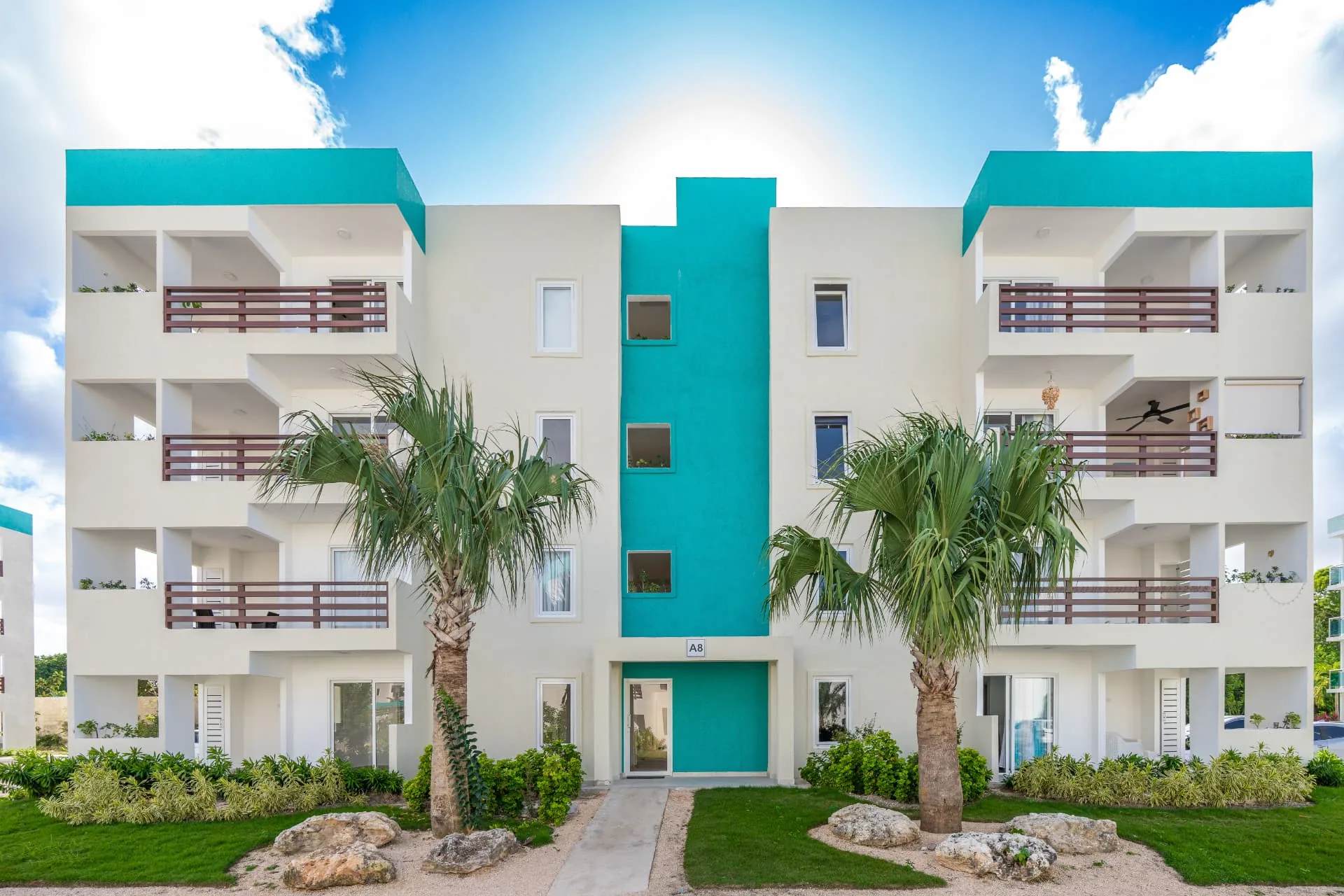 Four-storey condominium facade with turquoise accents, timber balcony railings and palms