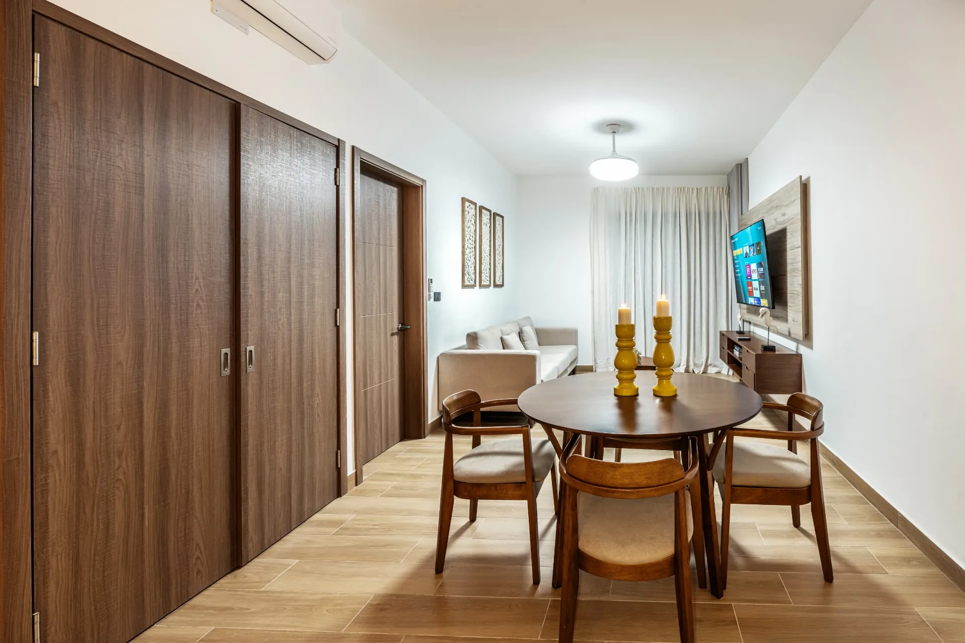Round mahogany dining table with four chairs, yellow candlesticks and sliding wardrobe doors along the hallway