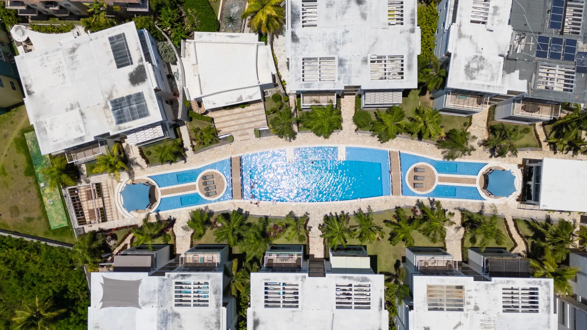 Top-down aerial of a long lagoon-style community pool framed by palms and white condominium blocks