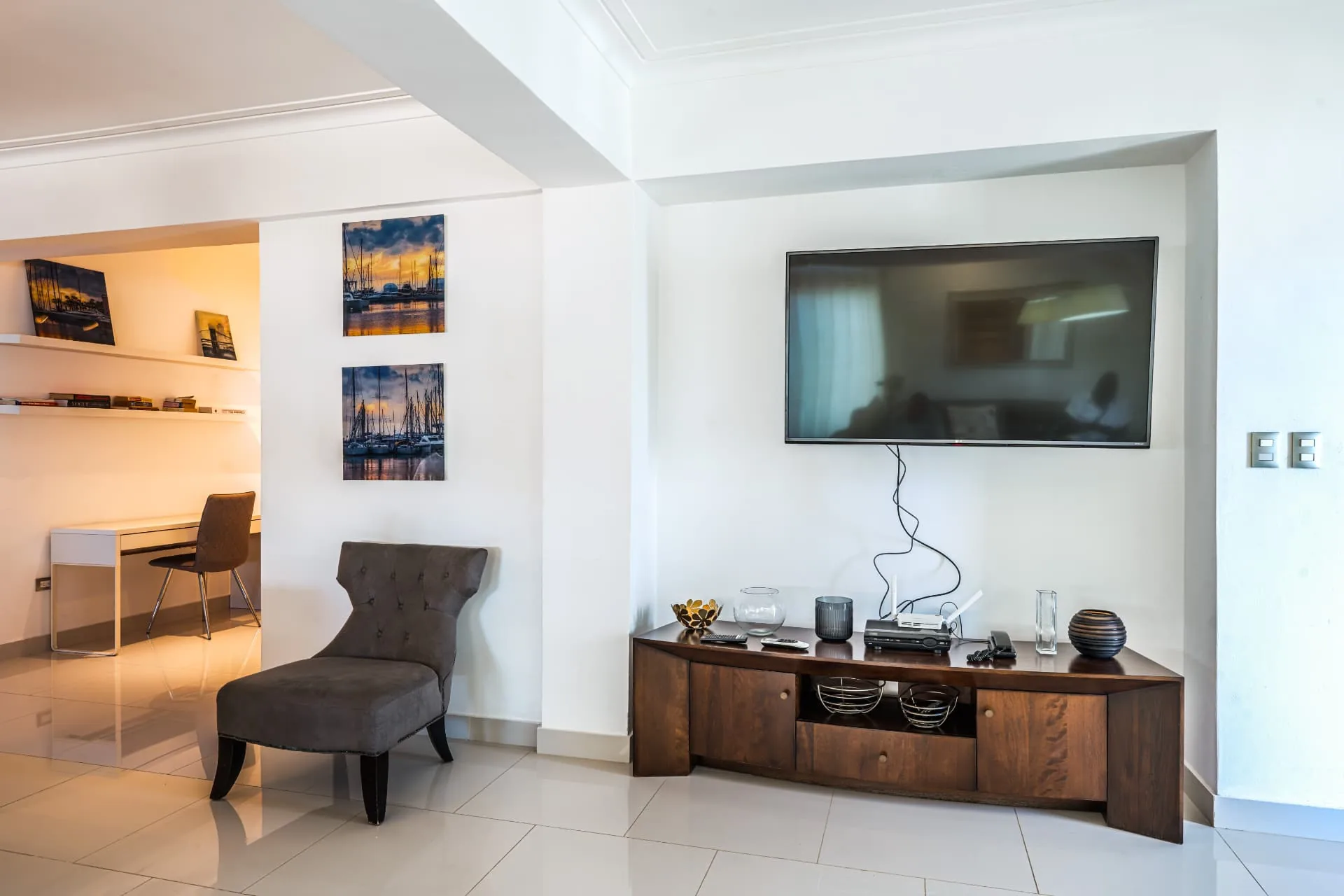 Condominium media wall with walnut console, accent chair and a lit study nook with floating shelves