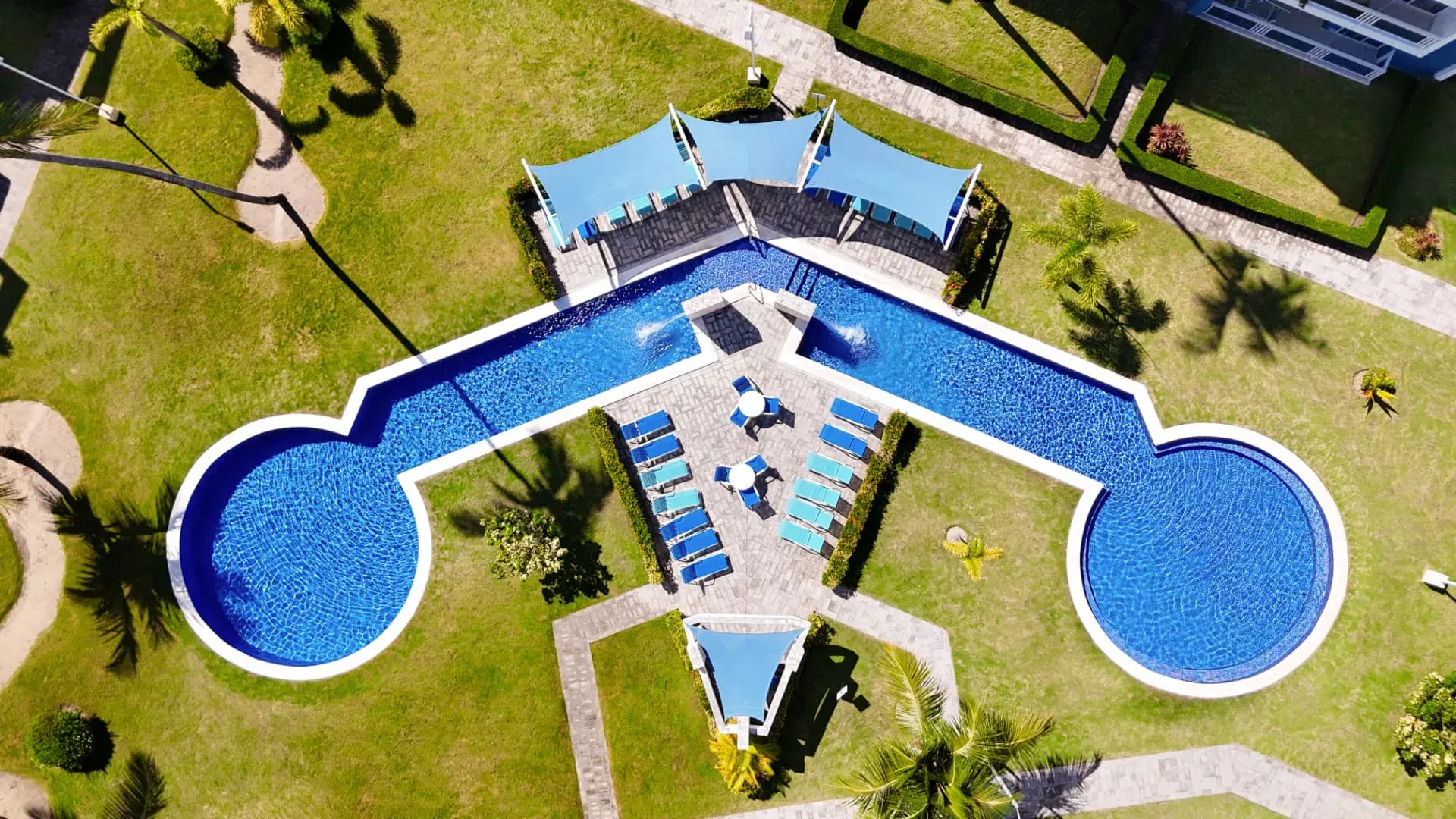 Overhead drone view of Eden's twin circular pools, shaded lounge decks and palm-lined gardens