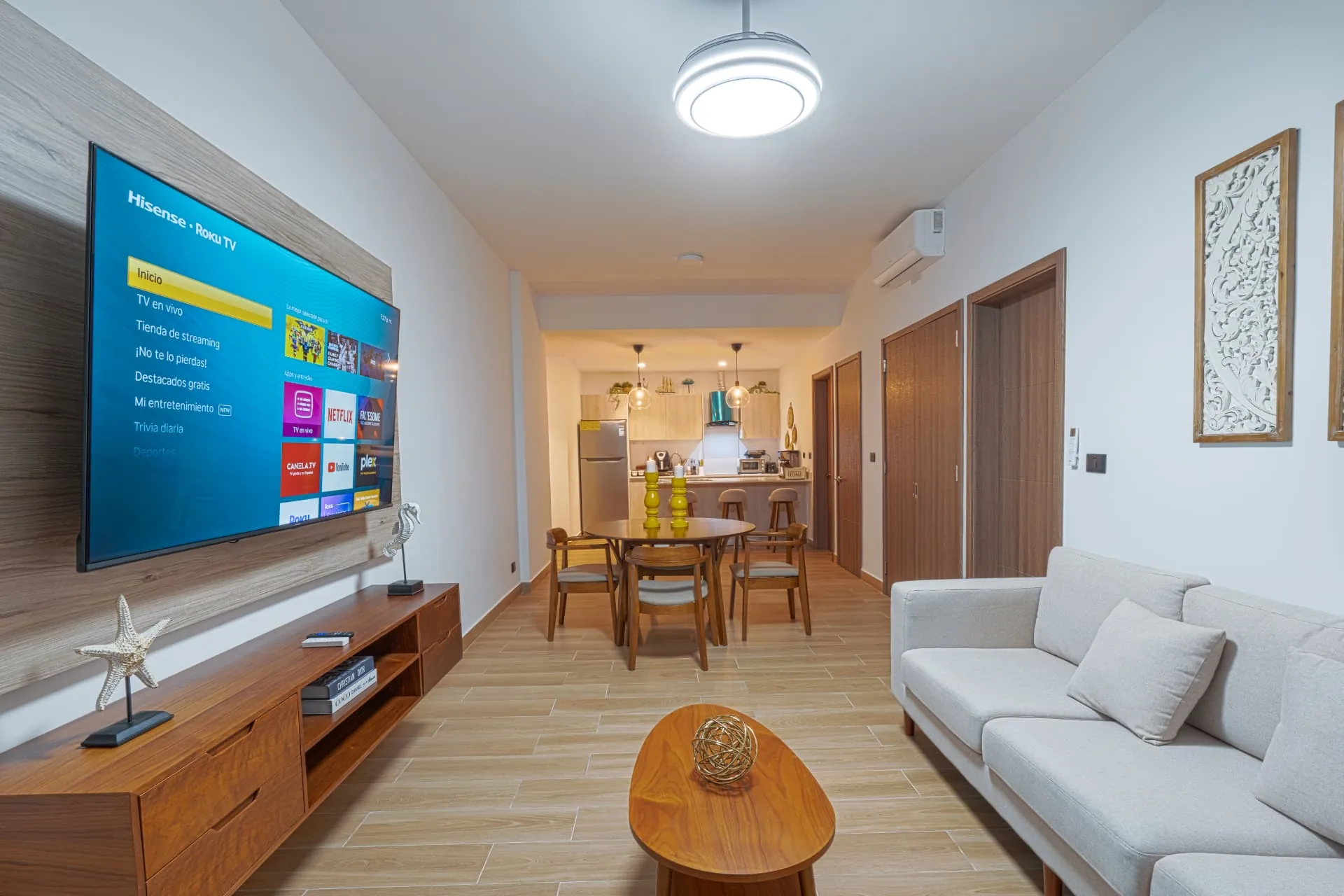 Open living room at DownTown with mounted television, timber media console, dining table and kitchen bar beyond