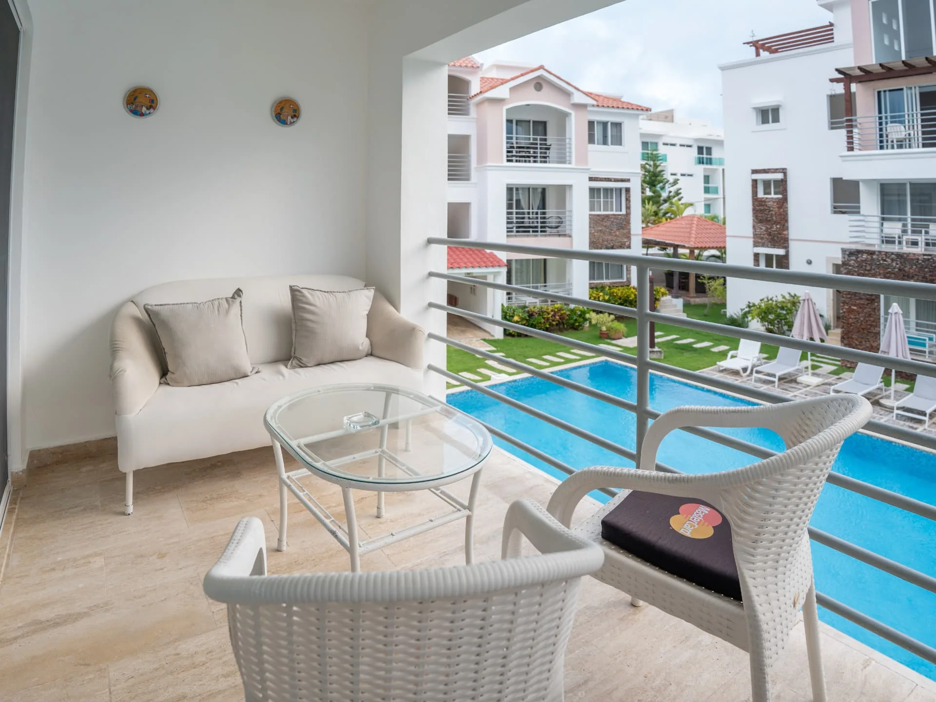 Private balcony with cream loveseat, woven armchairs and a glass table overlooking the pools and gardens