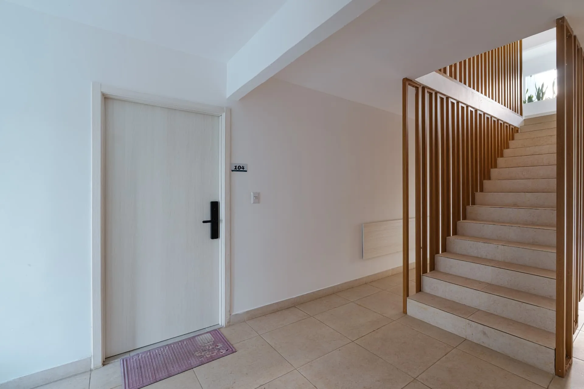 Condominium entry hall with white unit door and travertine stair behind a timber slatted screen