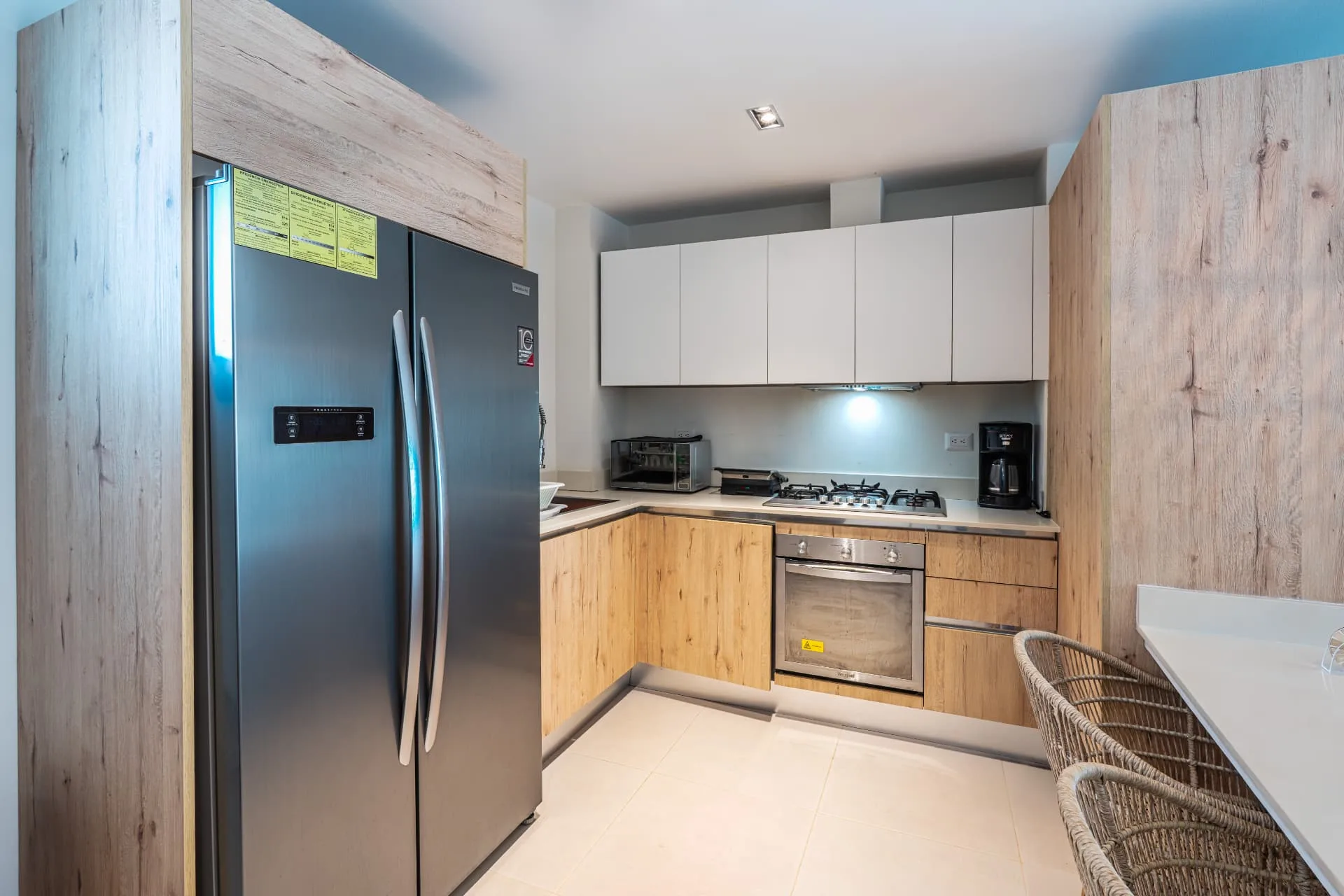 Compact kitchen with stainless steel refrigerator, oven, gas cooktop and pale upper cabinets