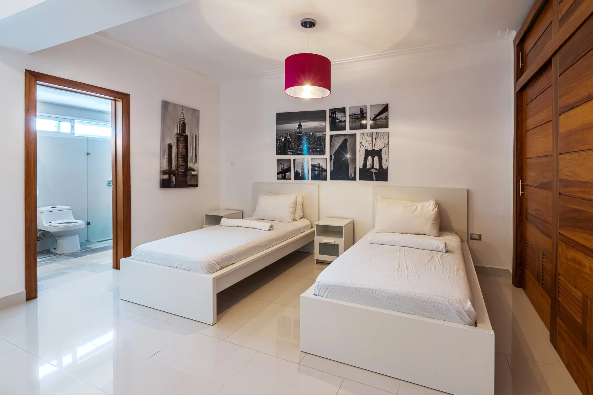 Twin guest bedroom with white bedframes, gallery wall and open door to a marble en-suite bathroom