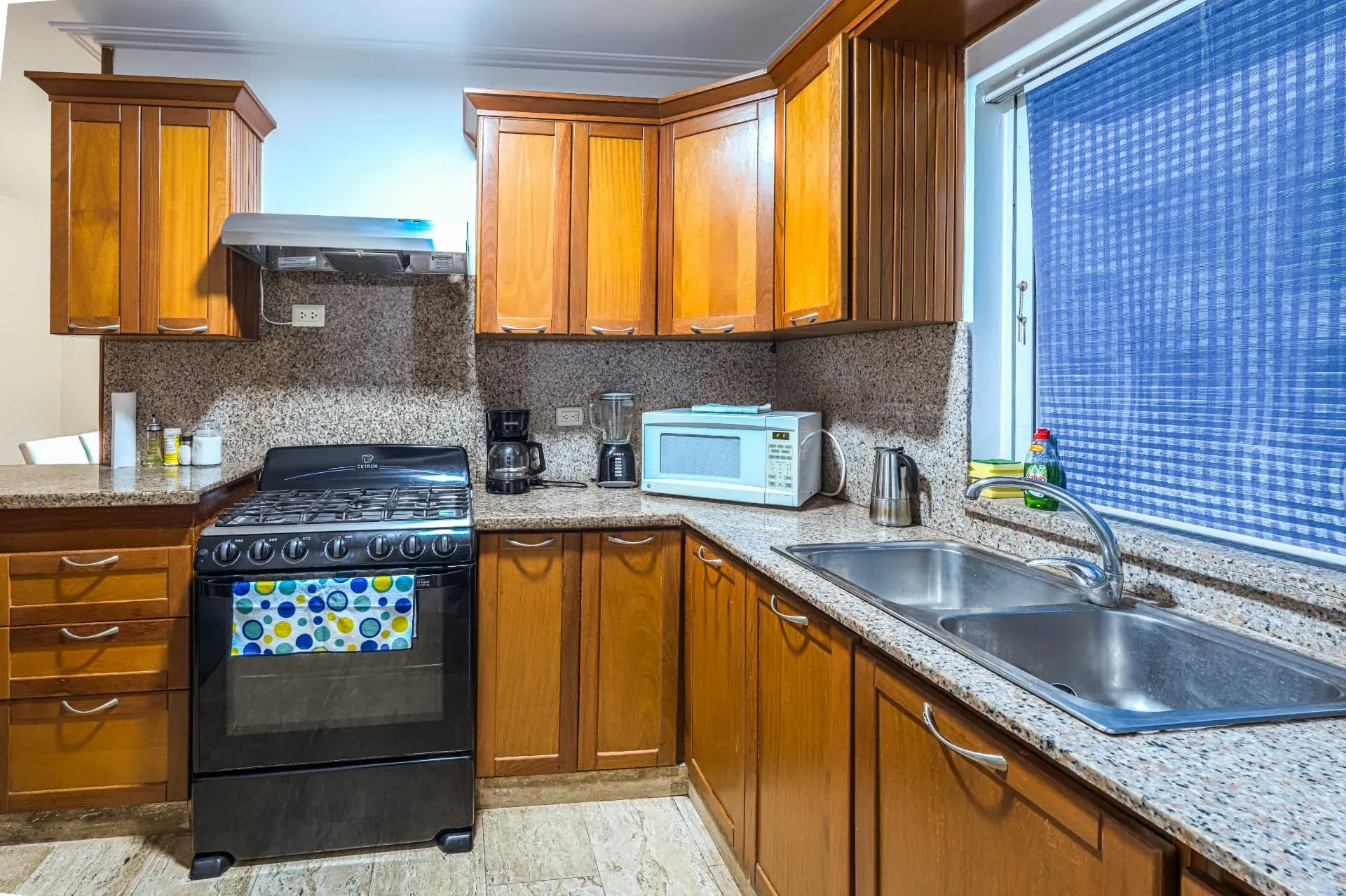 Kitchen with warm timber cabinetry, granite counters, gas range and a double stainless steel sink by the window