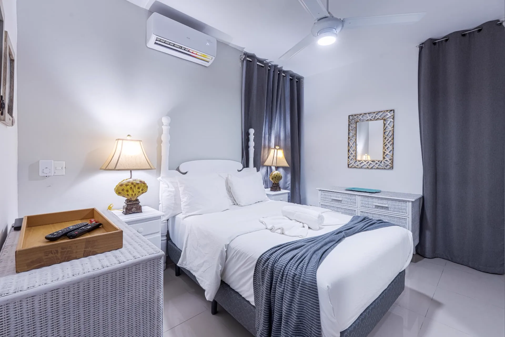 Primary bedroom with white four-poster bed, shell table lamps, ceiling fan and charcoal blackout curtains