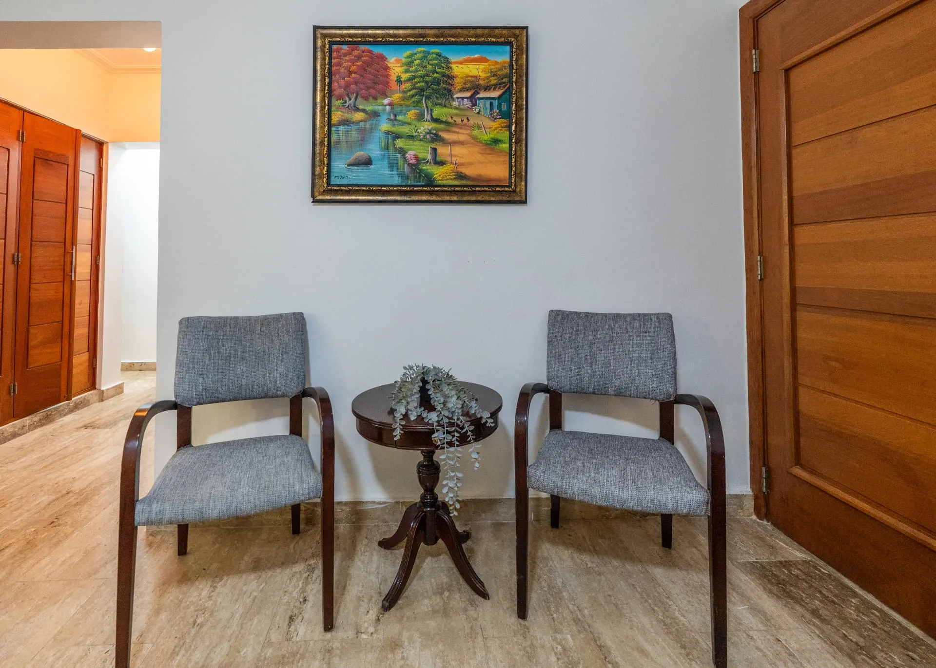 Entry sitting nook with two grey armchairs, a round mahogany side table and framed landscape painting