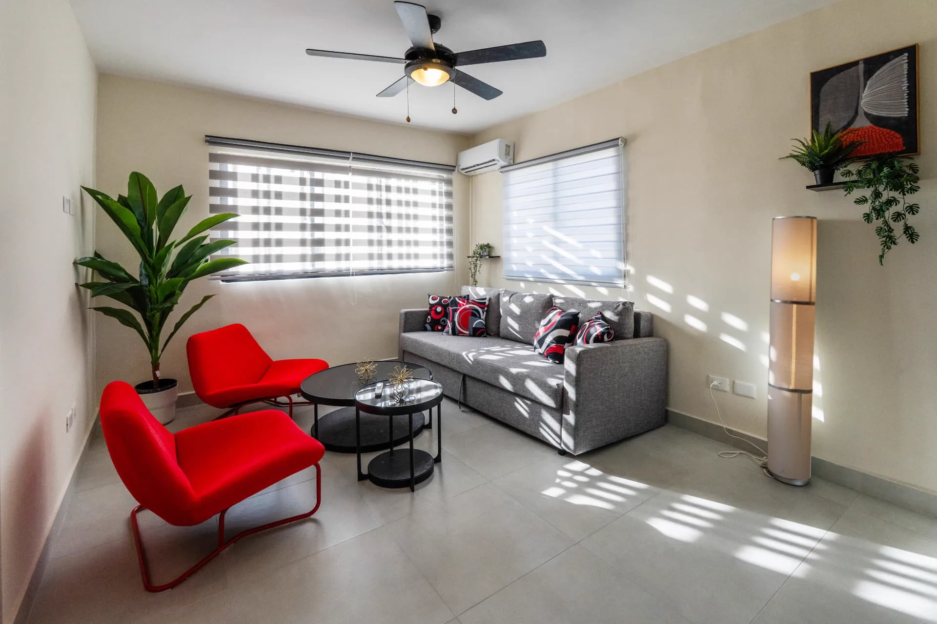 Sunlit living room at Epic Sun with grey sofa, two red accent chairs and nested black coffee tables