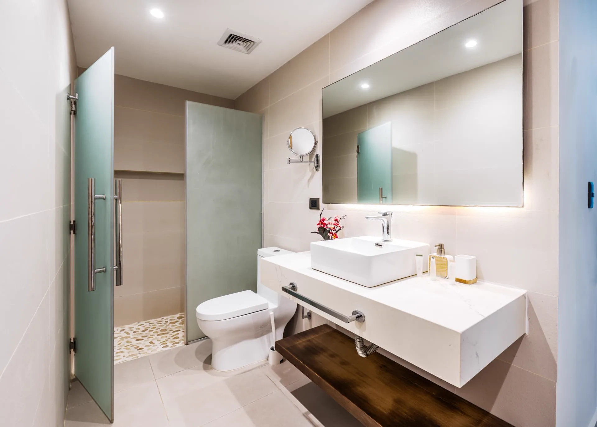 Guest bathroom with frosted glass shower screen, vessel sink on a stone counter and wide mirror
