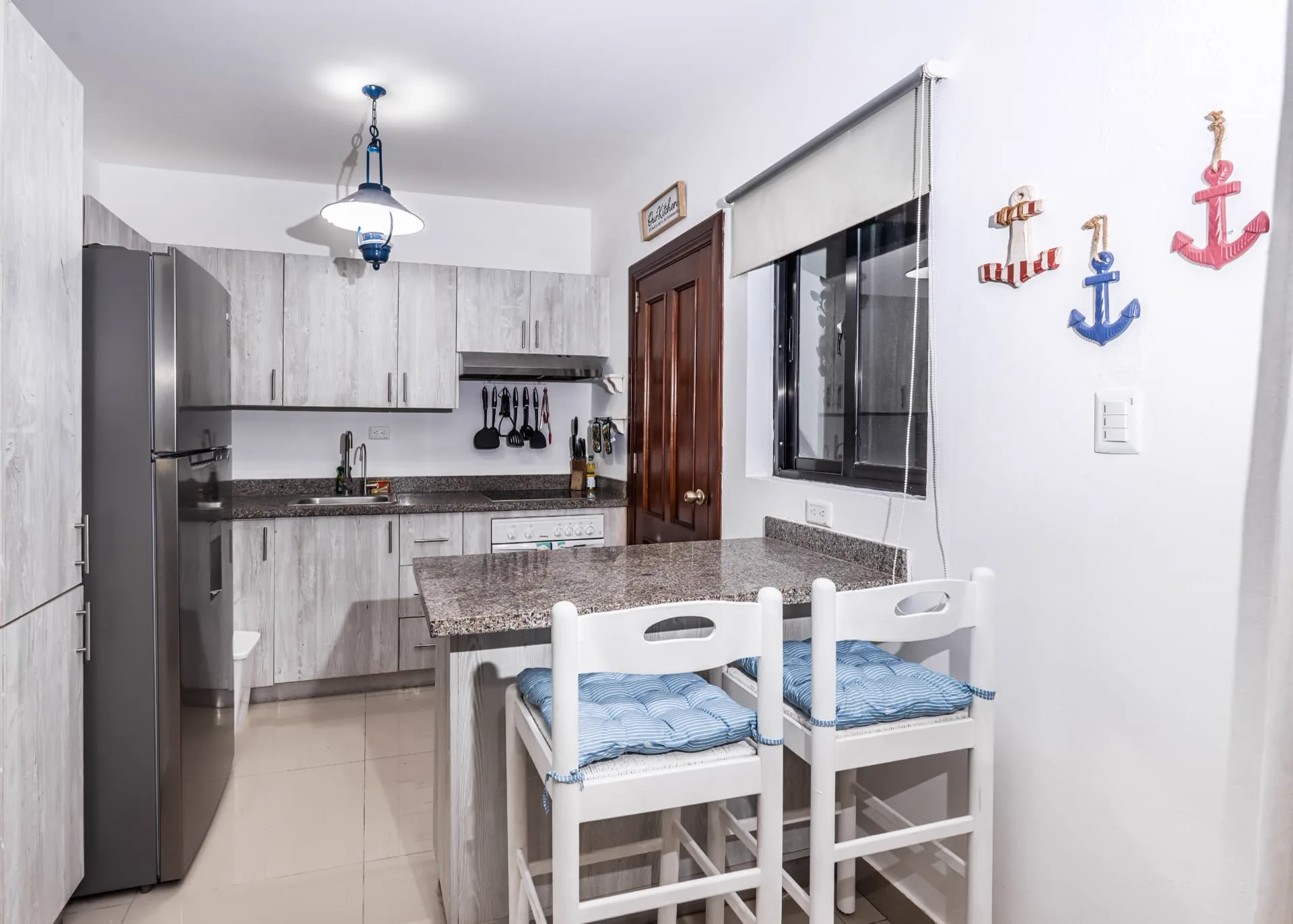 Kitchen with pale timber cabinetry, granite breakfast bar with striped cushioned stools and anchor wall decor