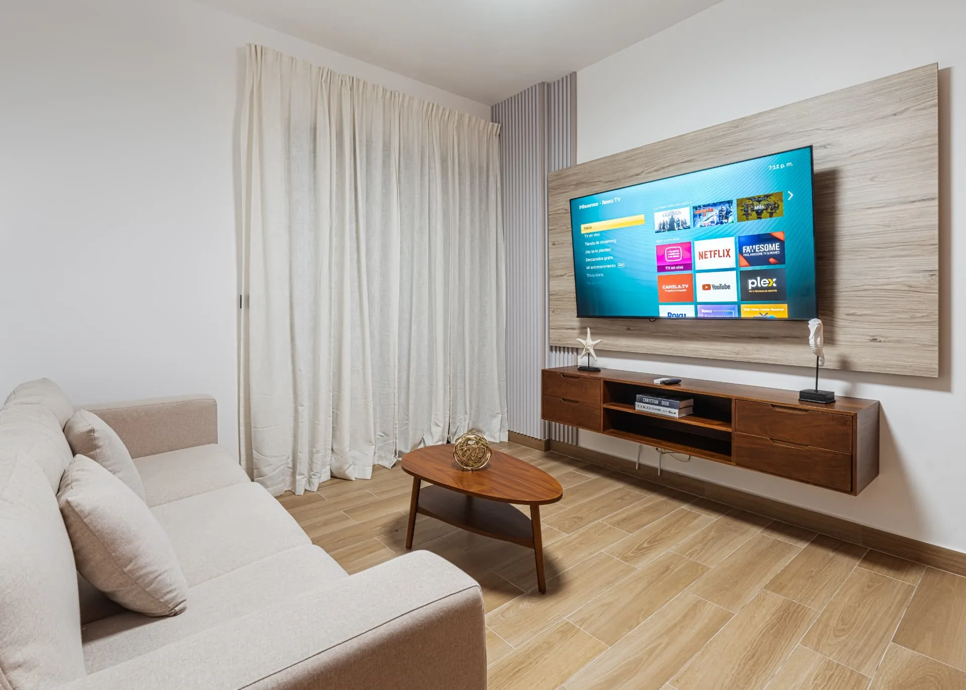 Living room with linen sofa, oval walnut coffee table and a wall-mounted television on a timber panel