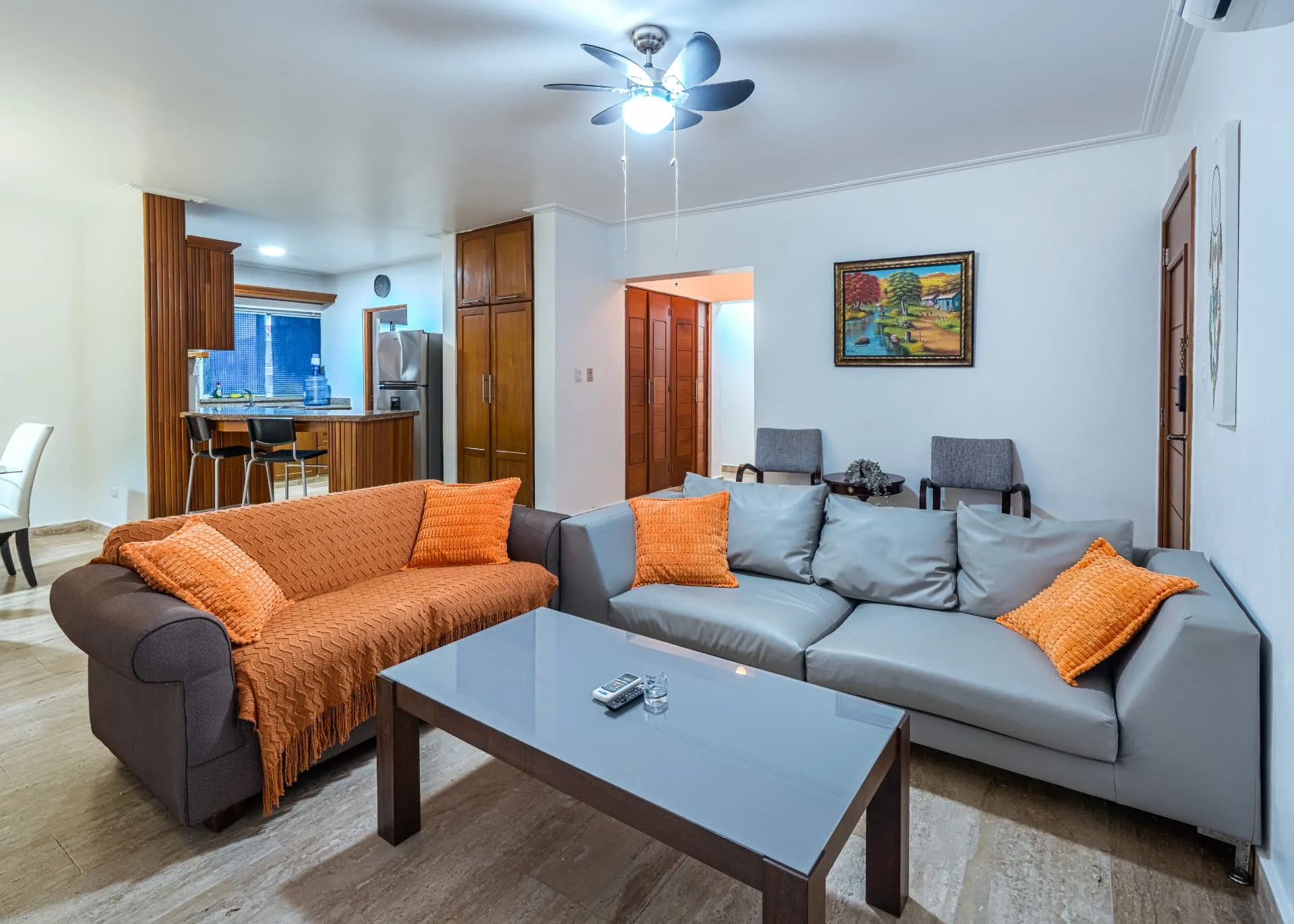Open living room at Corte Sea with grey and orange sofas, glass coffee table and an open sightline to the kitchen bar