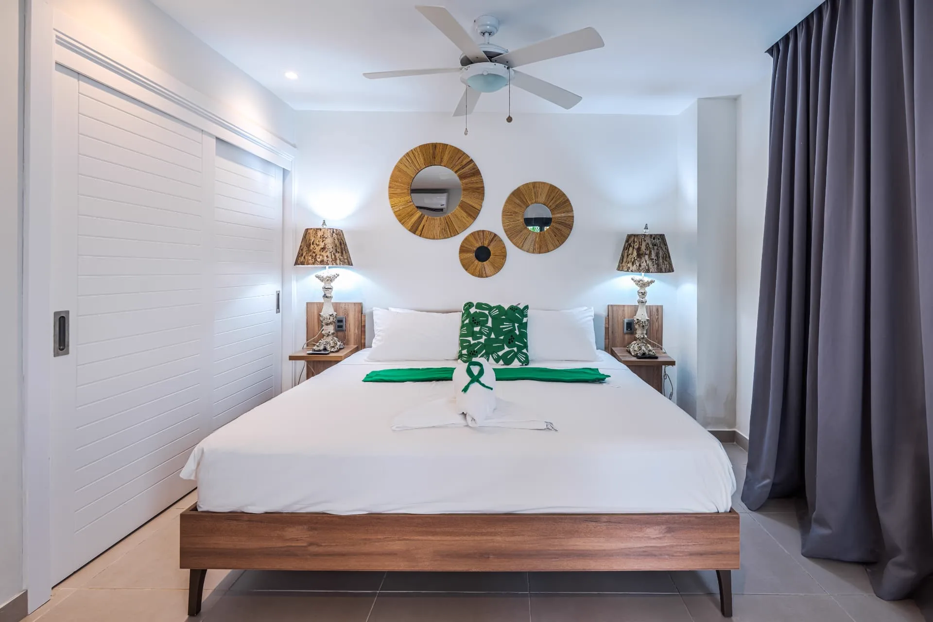 Second bedroom with white bedding, green accents and three woven sunburst mirrors above the bed