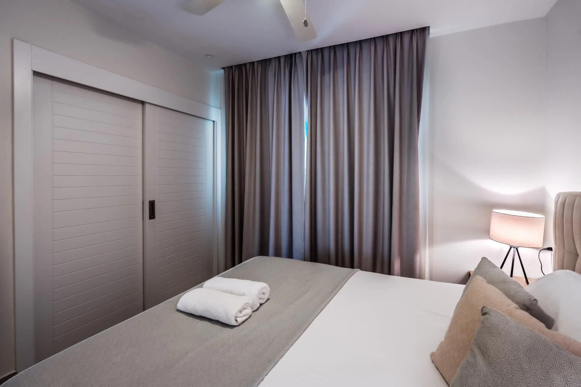 Bedroom detail with louvred sliding closet doors, folded towels on the bed and lamp light
