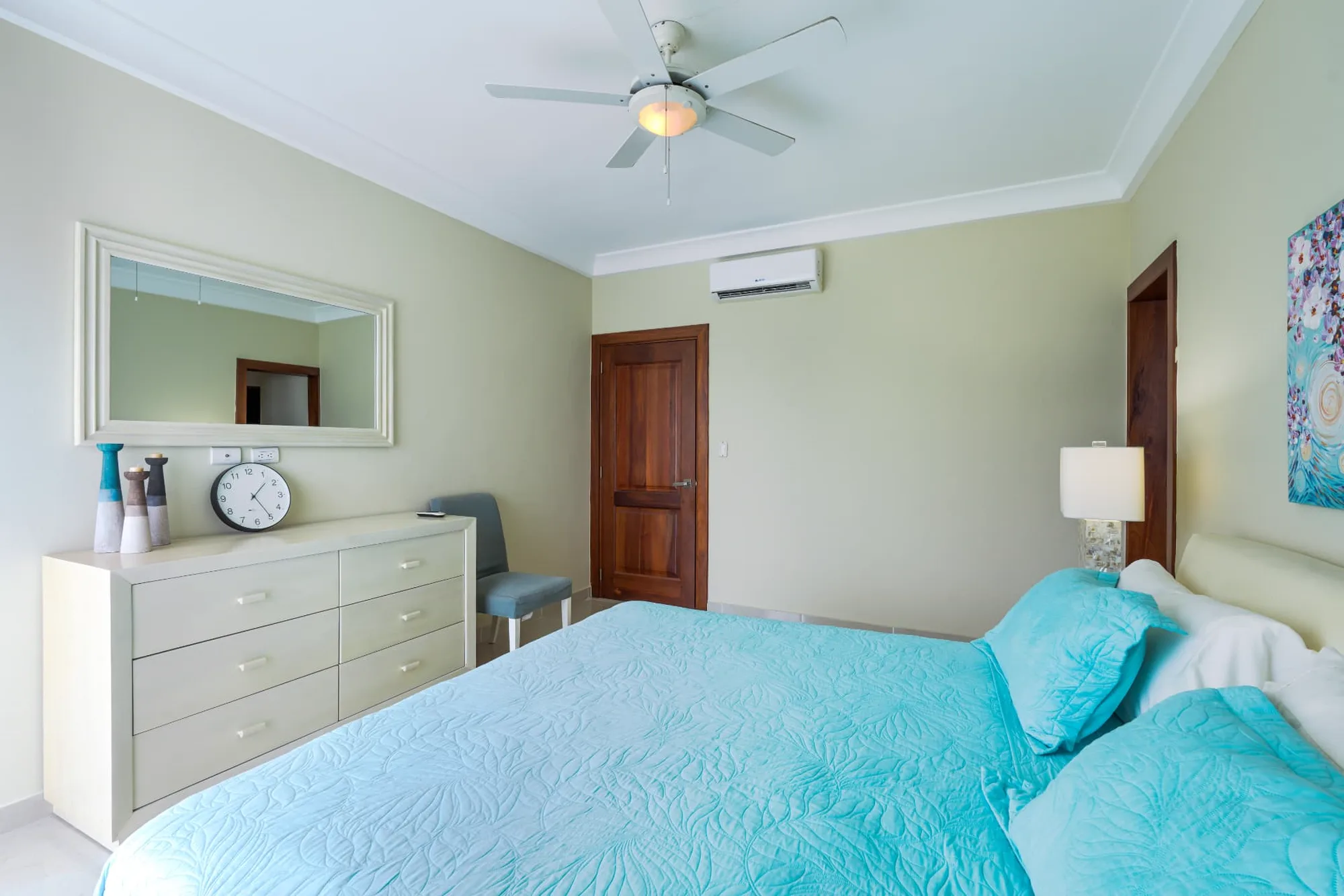 Primary bedroom from the balcony side showing the dresser, framed mirror and turquoise bedding