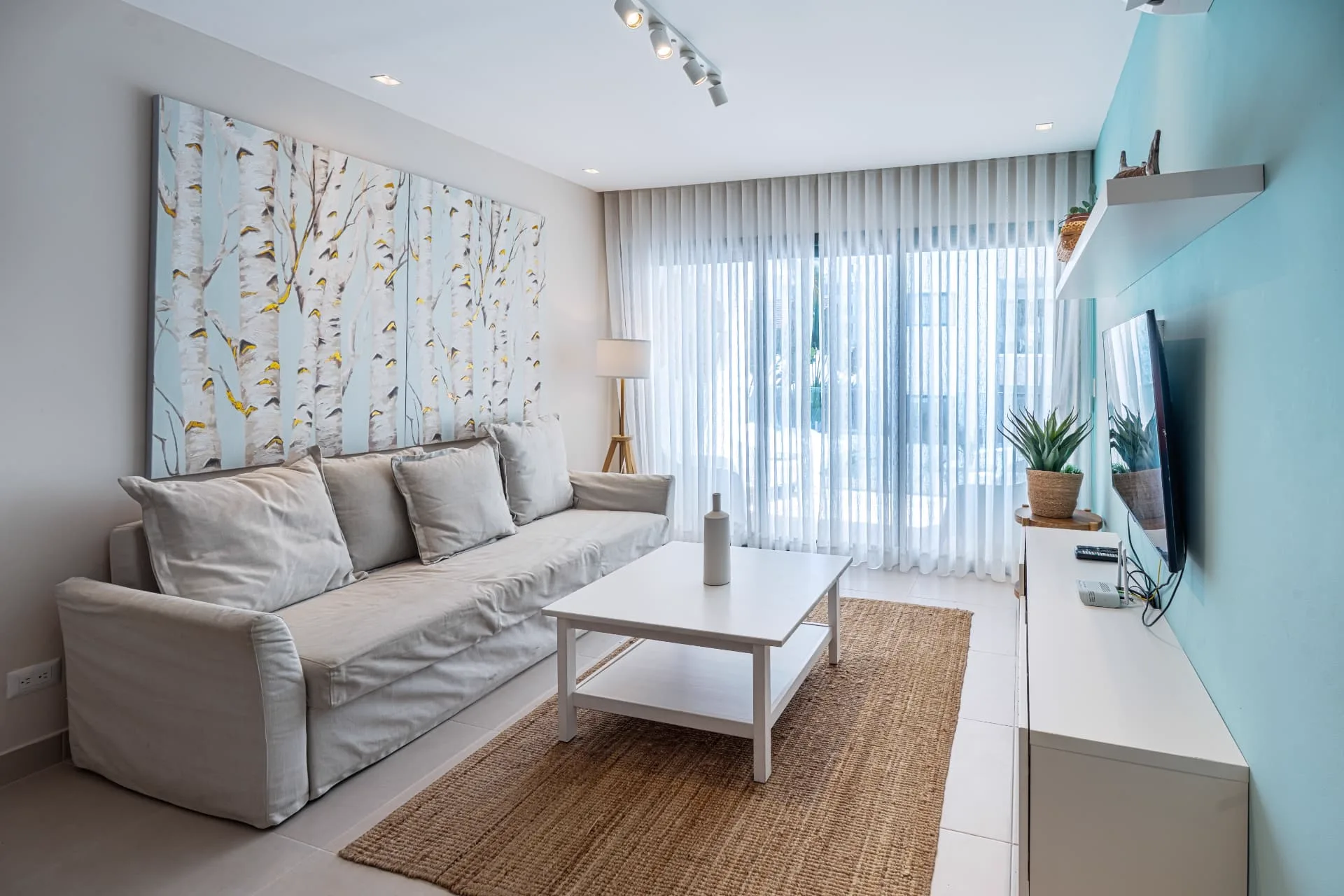 Living room with linen sofa, birch-forest canvas, jute rug and wall-mounted TV on a turquoise feature wall