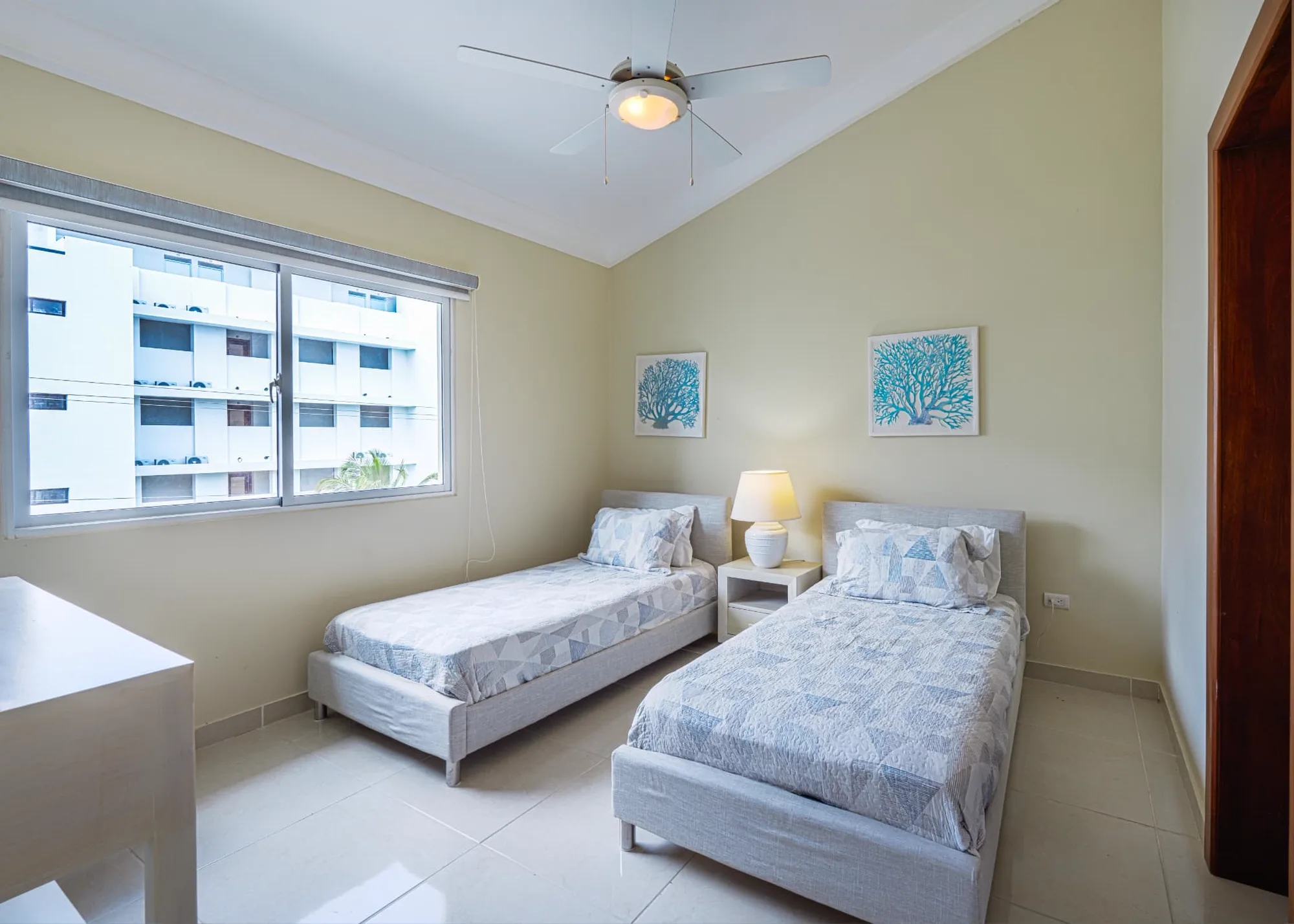 Twin guest bedroom with two upholstered beds, patterned quilts, coral prints and a bright window