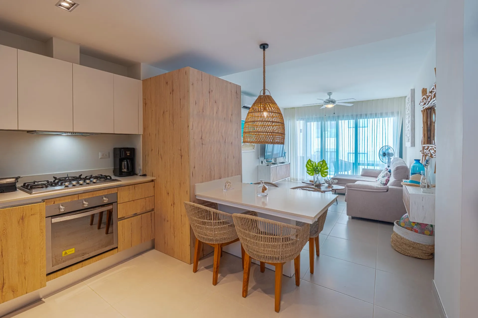 Open kitchen with timber cabinetry, gas cooktop and a white dining bar with woven rattan chairs