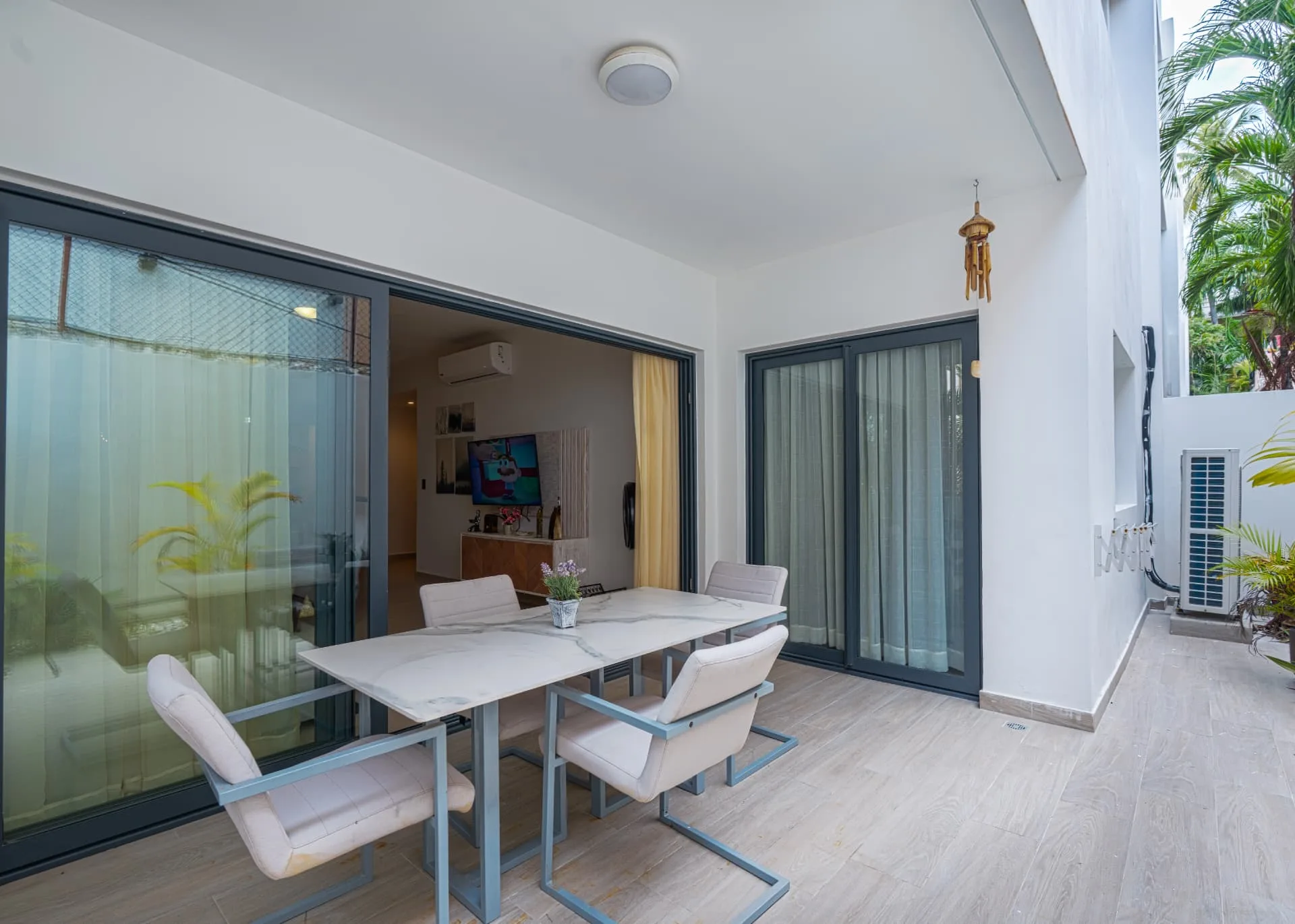 Covered private terrace with marble dining table and cushioned chairs beside sliding glass doors