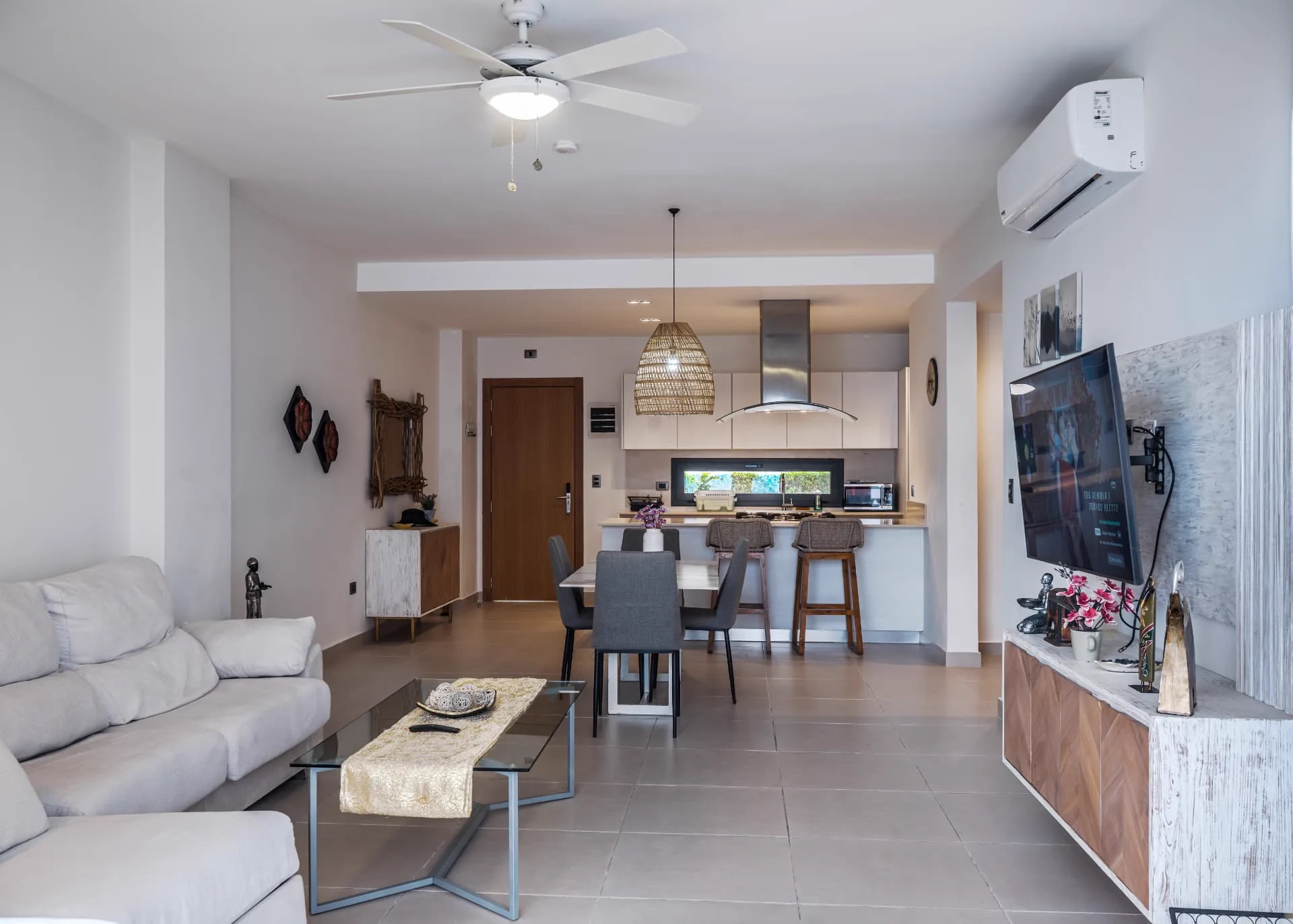 Bright open-plan living room with pale sofa, glass coffee table, dining table and kitchen beyond