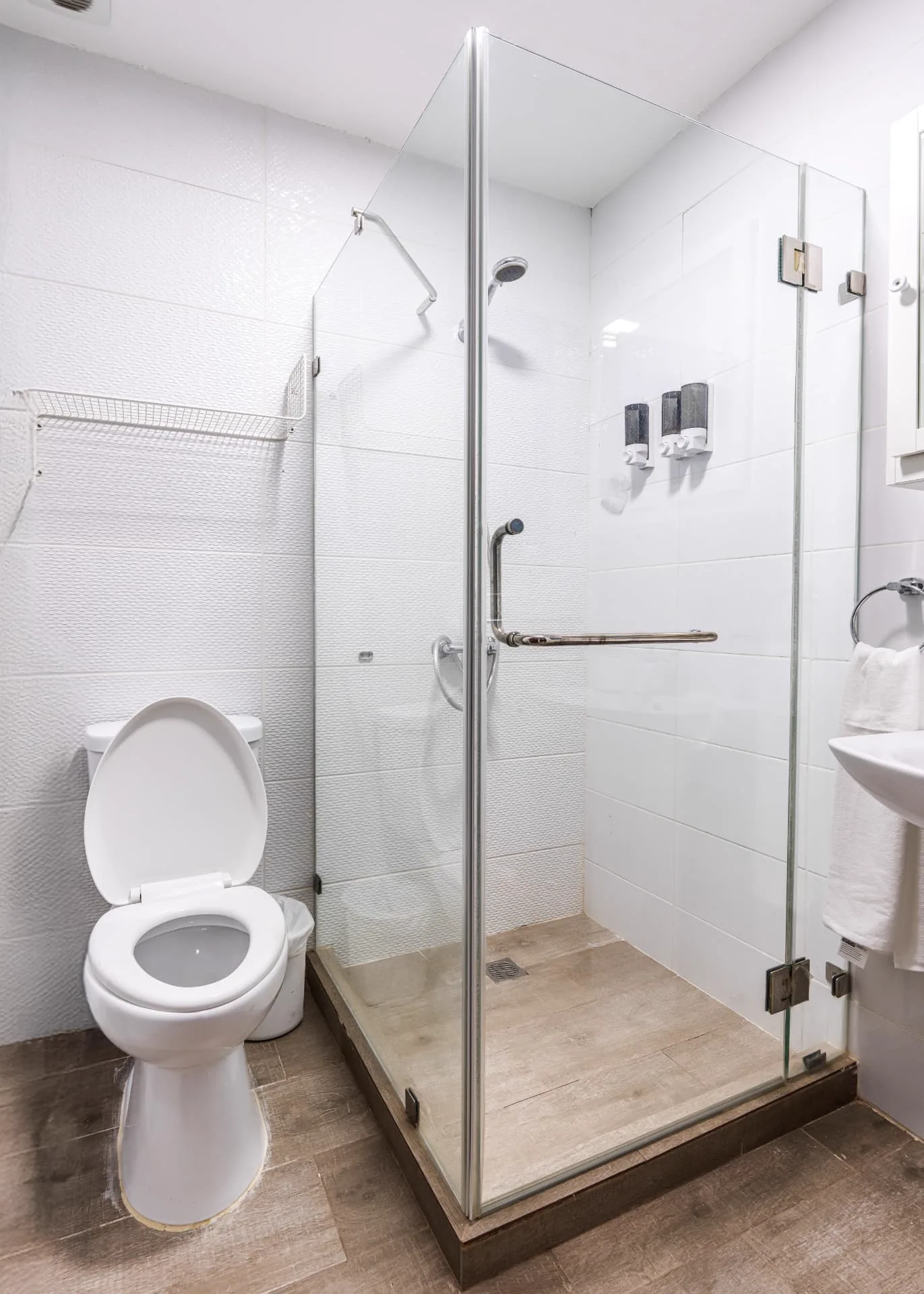 Guest bathroom with textured white tile, walk-in glass shower with fixed screen and hanging towels