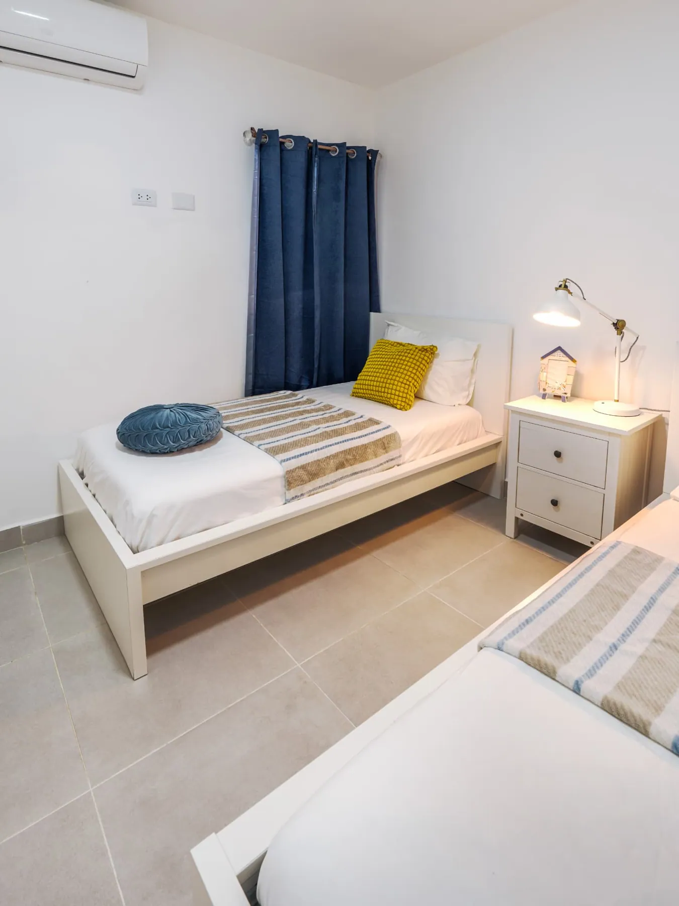 Twin bedroom from the window side with navy curtains, mustard cushions and bedside lamp