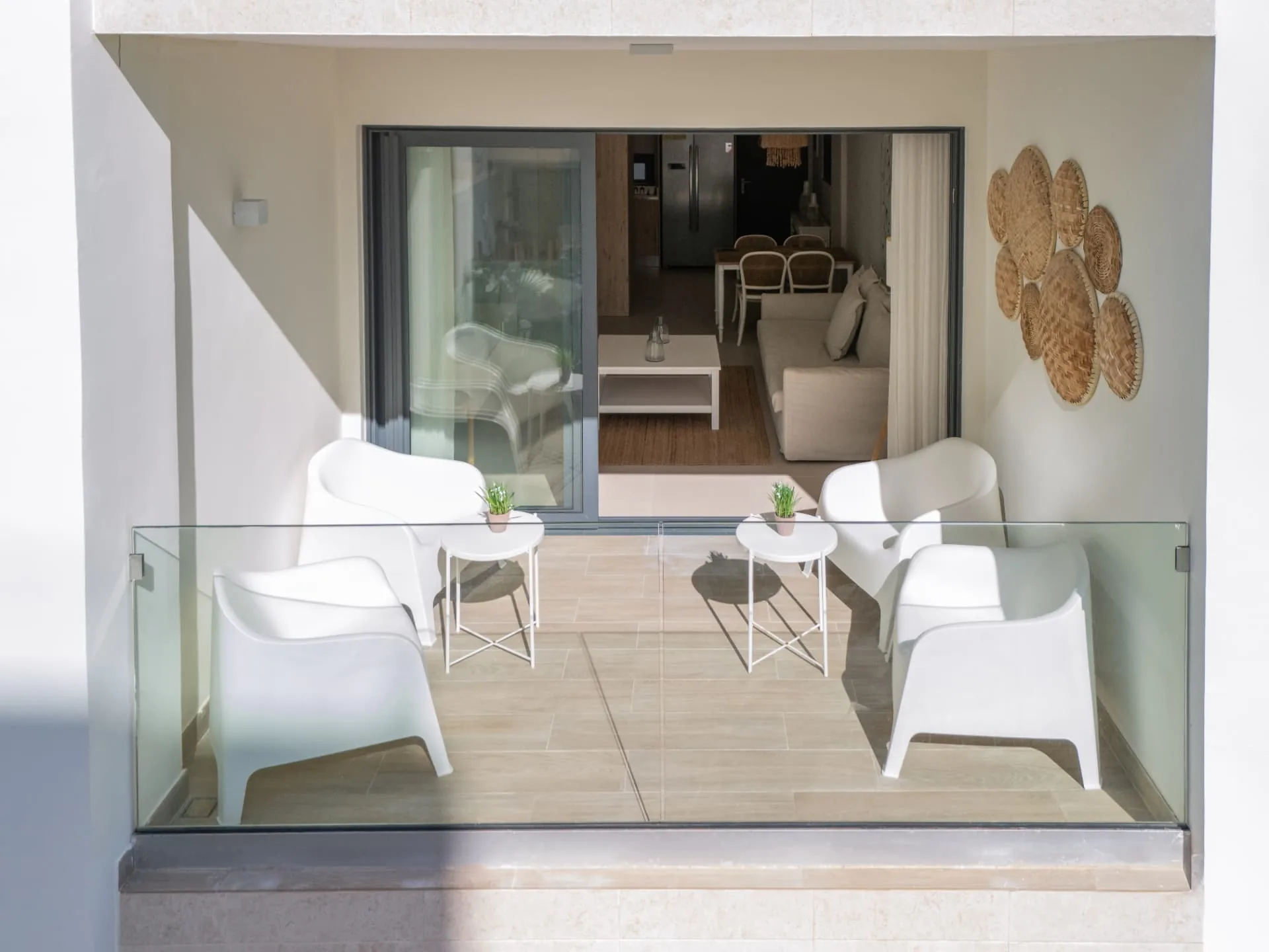 Garden terrace with white lounge chairs and glass balustrade opening into a bright living room