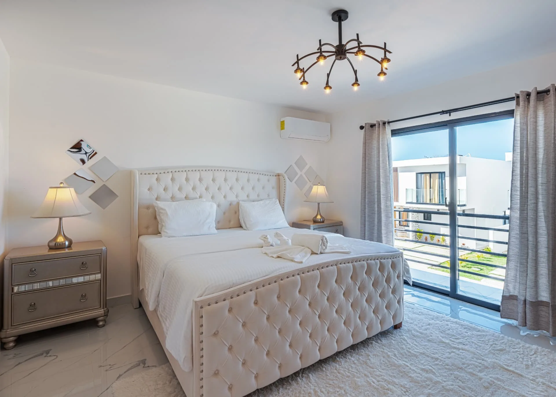 Primary bedroom with tufted upholstered bed, marble floors and sliding doors to a balcony