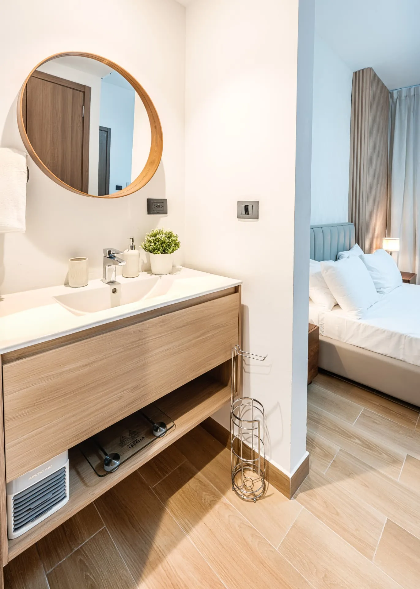 Timber vanity with round mirror beside a bedroom with a blue upholstered headboard